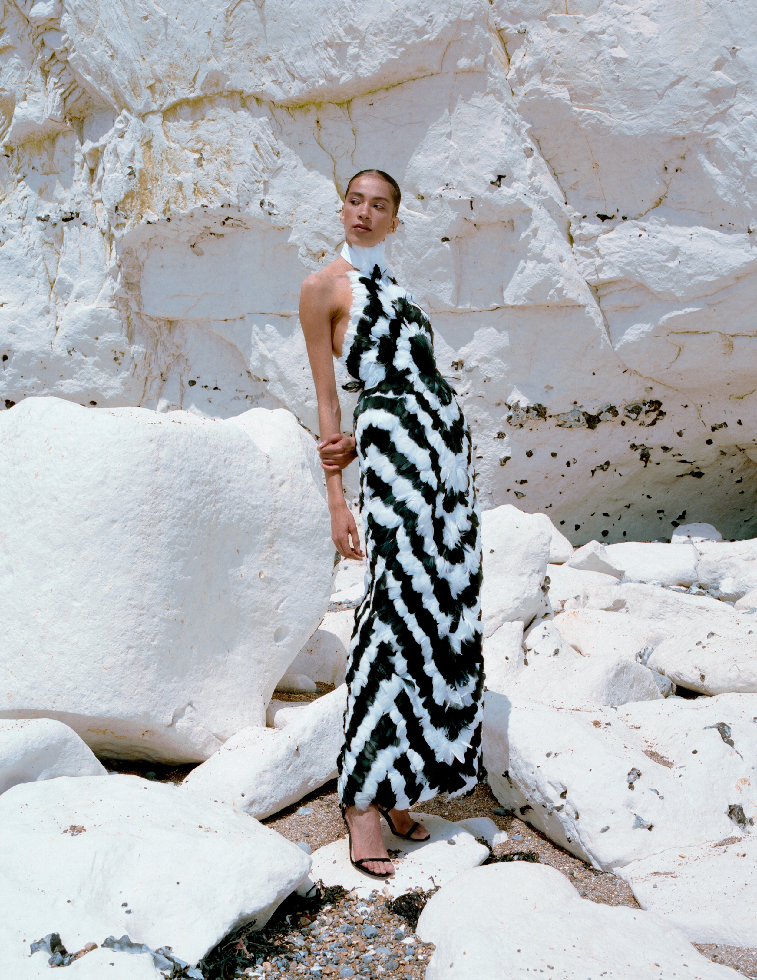 mixed race woman wears a luxury halter neck evening dress covered in black and white feathers