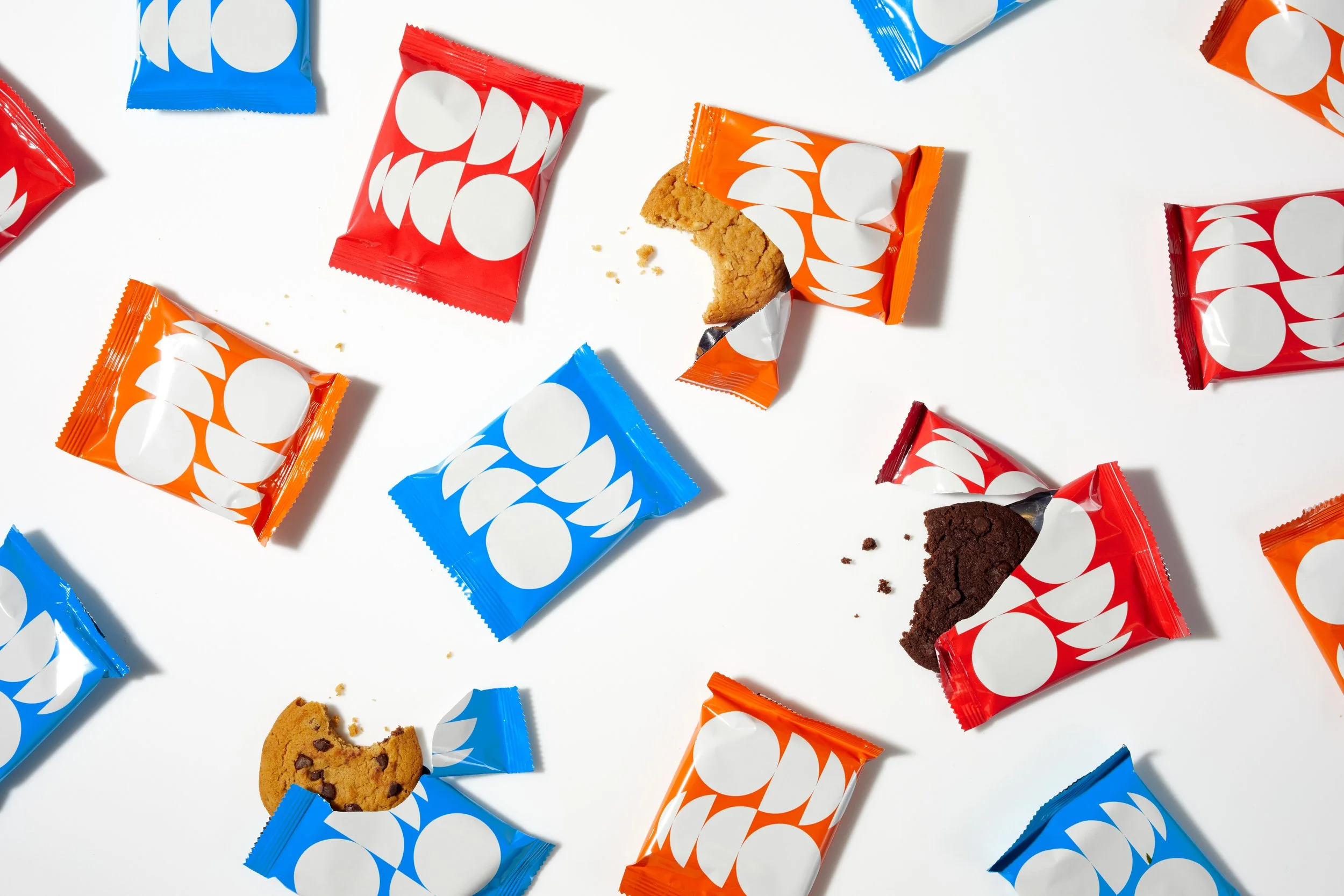 Scattered cookies in colorful wrappers on a white surface, with some cookie crumbs.