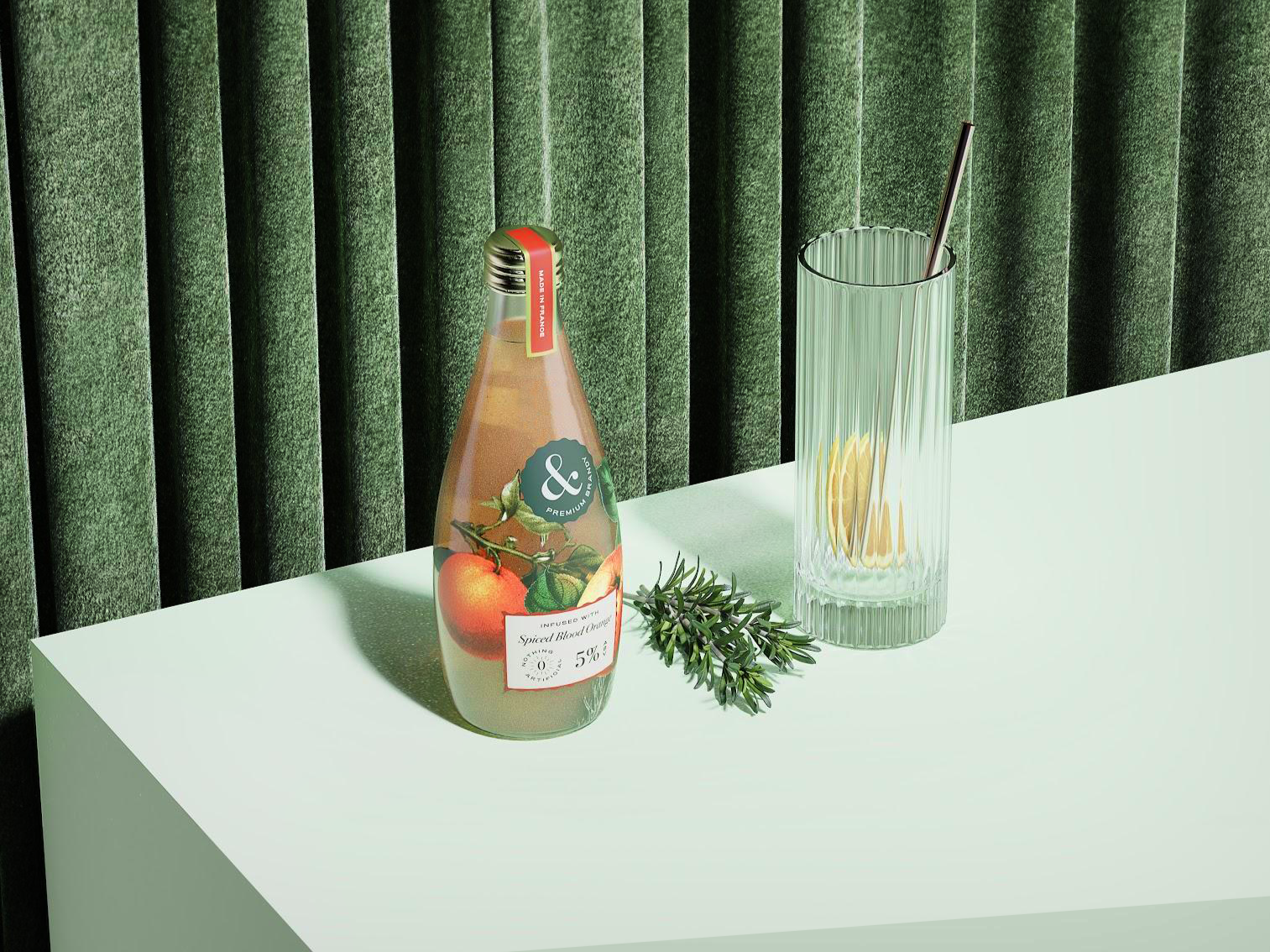 A clear glass bottle of Spiced Blood Orange juice, a sprig of rosemary, and a tall drinking glass with a straw and lemon slices on a white table, against a green curtain background.