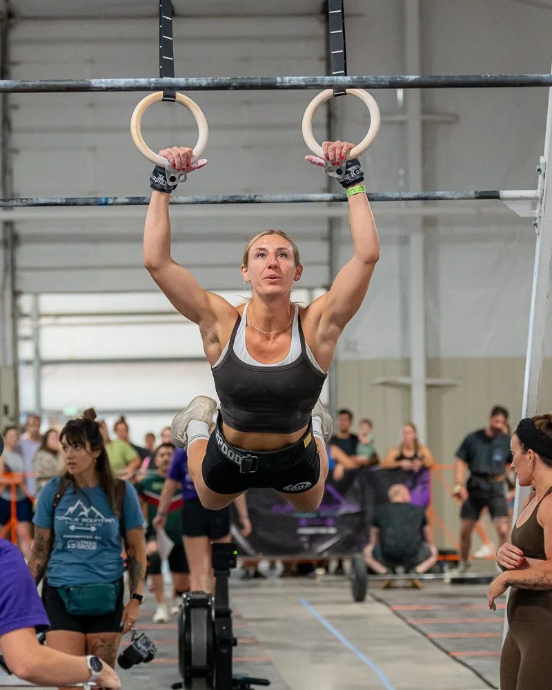 A woman in a red sports bra and matching shorts lifting a barbell during a weightlifting competition.