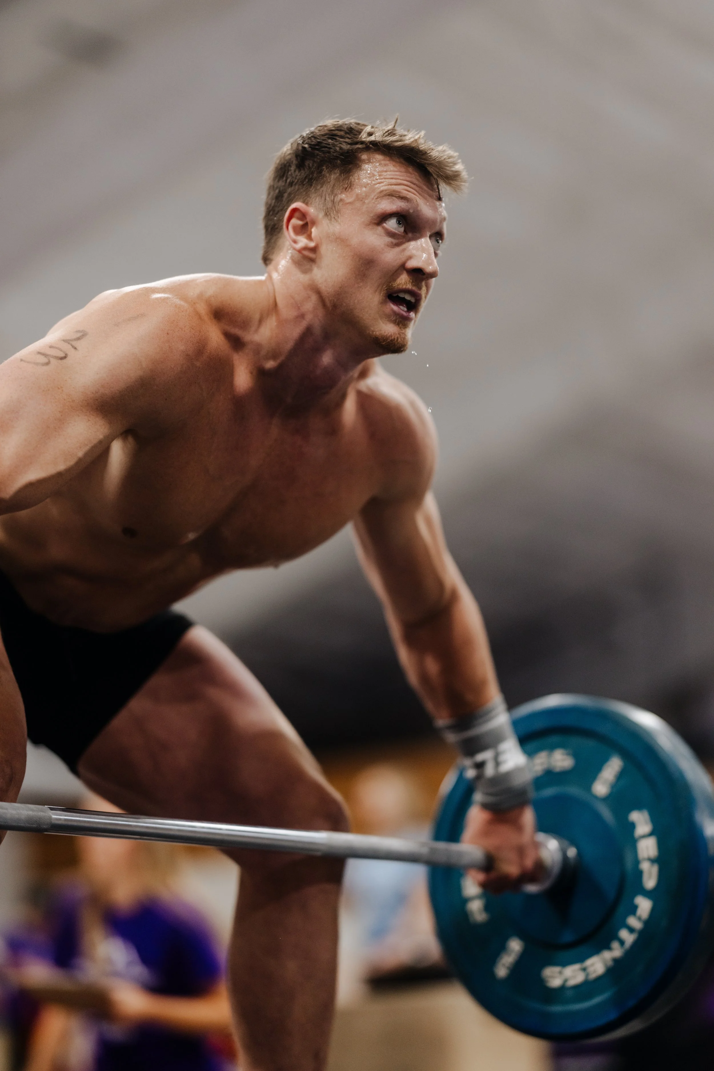 A man lifting a barbell overhead in a gym during a weightlifting competition.