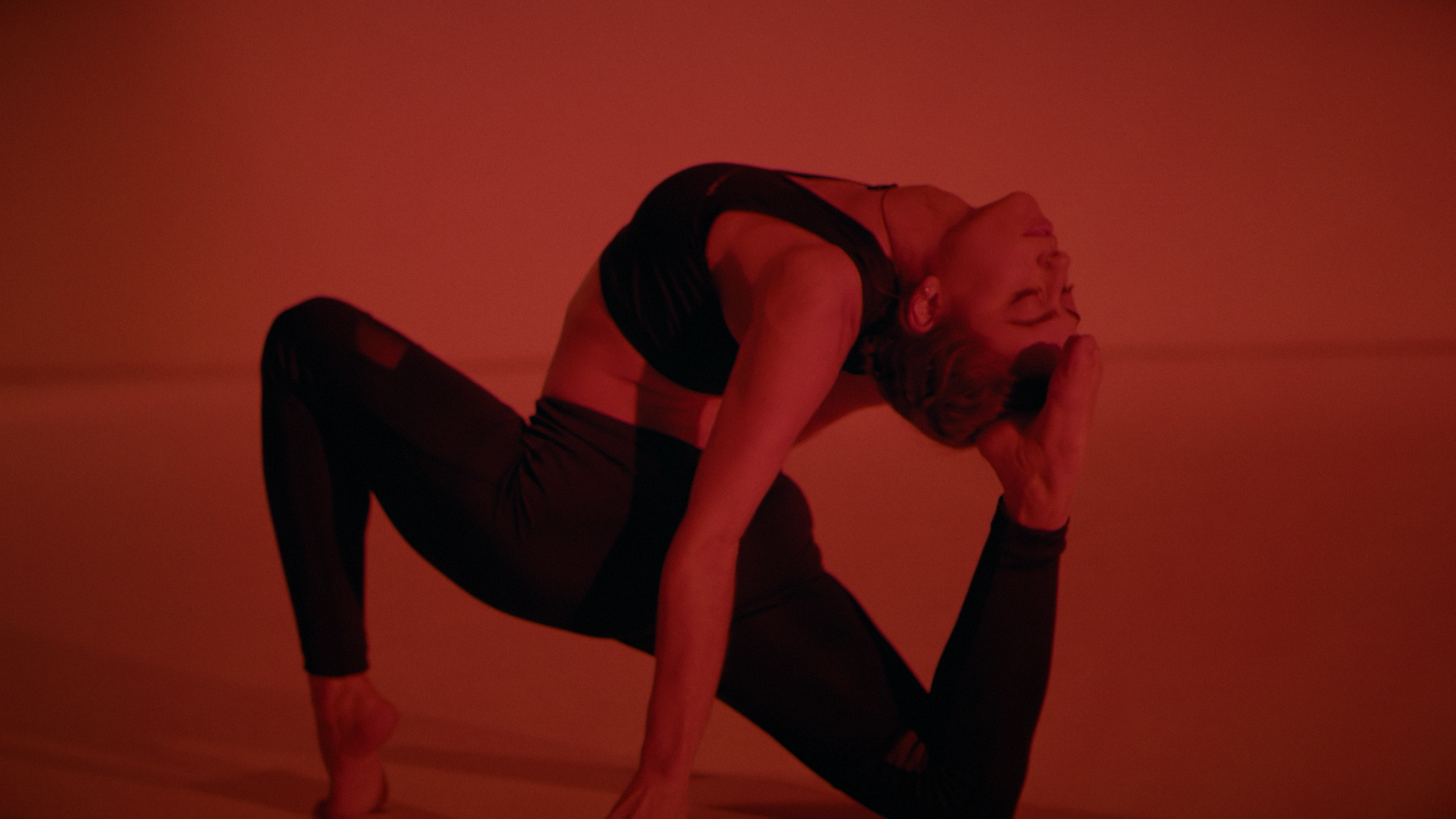 A woman practicing yoga in a twist pose on a red background.