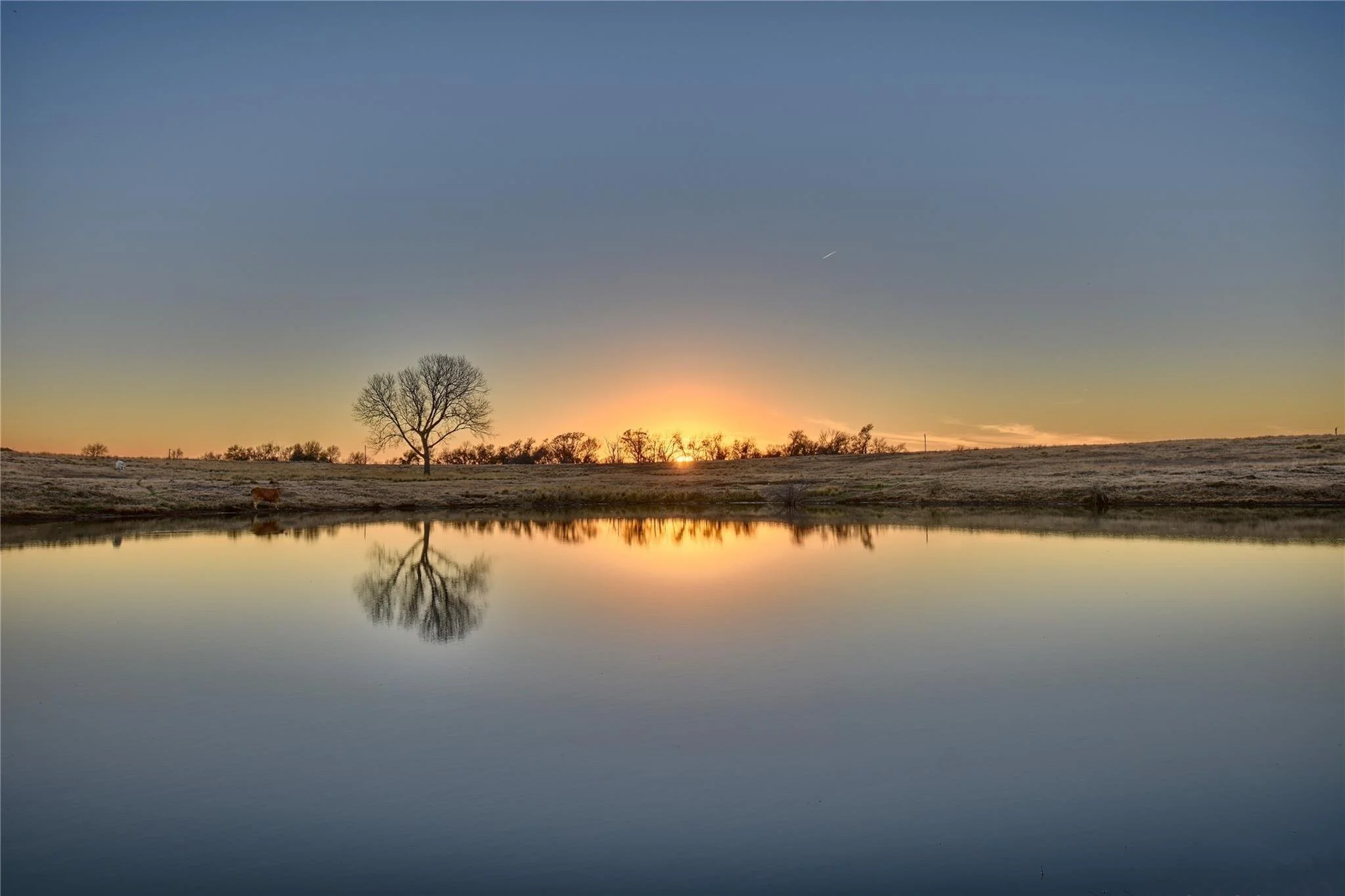 Sunset over a Brenham Texas ranch pond with calm water reflections and open pasture in the central texas countryside