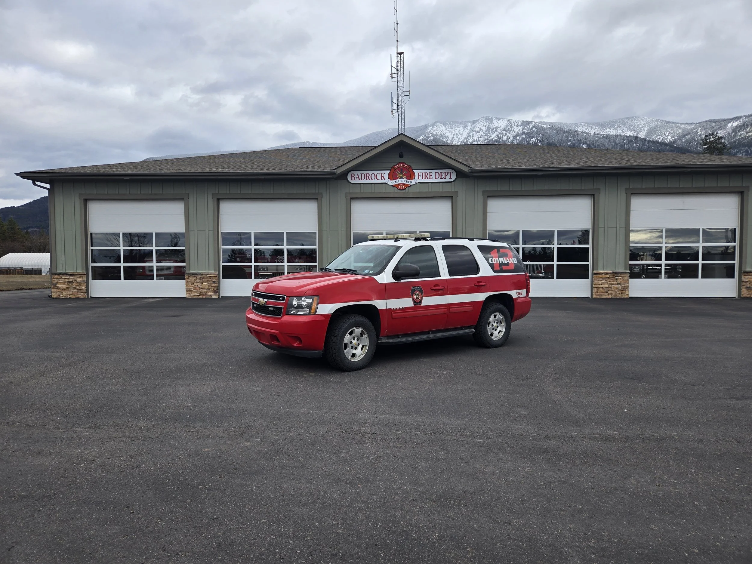 Red fire department command vehicle parked in front of Badrock Fire Department building with mountain scenery in the background.