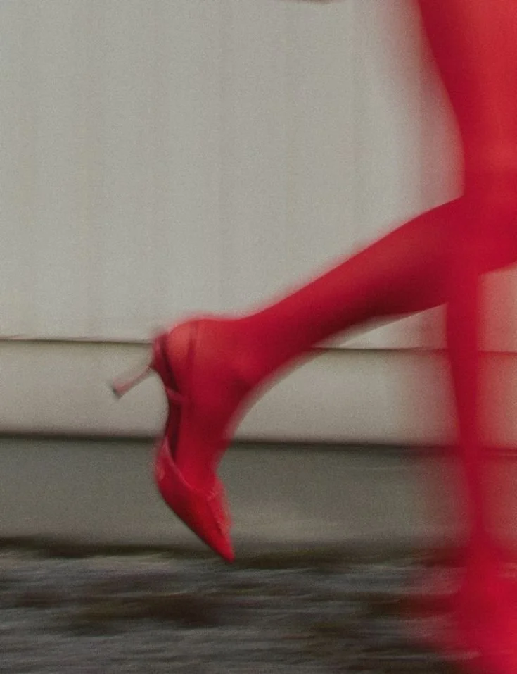 Close-up of a person wearing red high-heeled shoes and red tights, stepping forward.