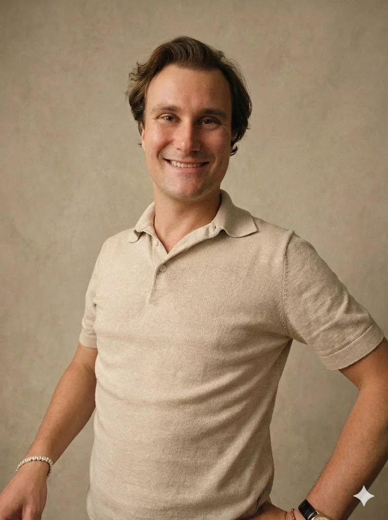 Ein Mann trägt ein beige Polo-Shirt, hat braune, wellige Haare und lächelt freundlich, steht vor einer neutralen Wand.