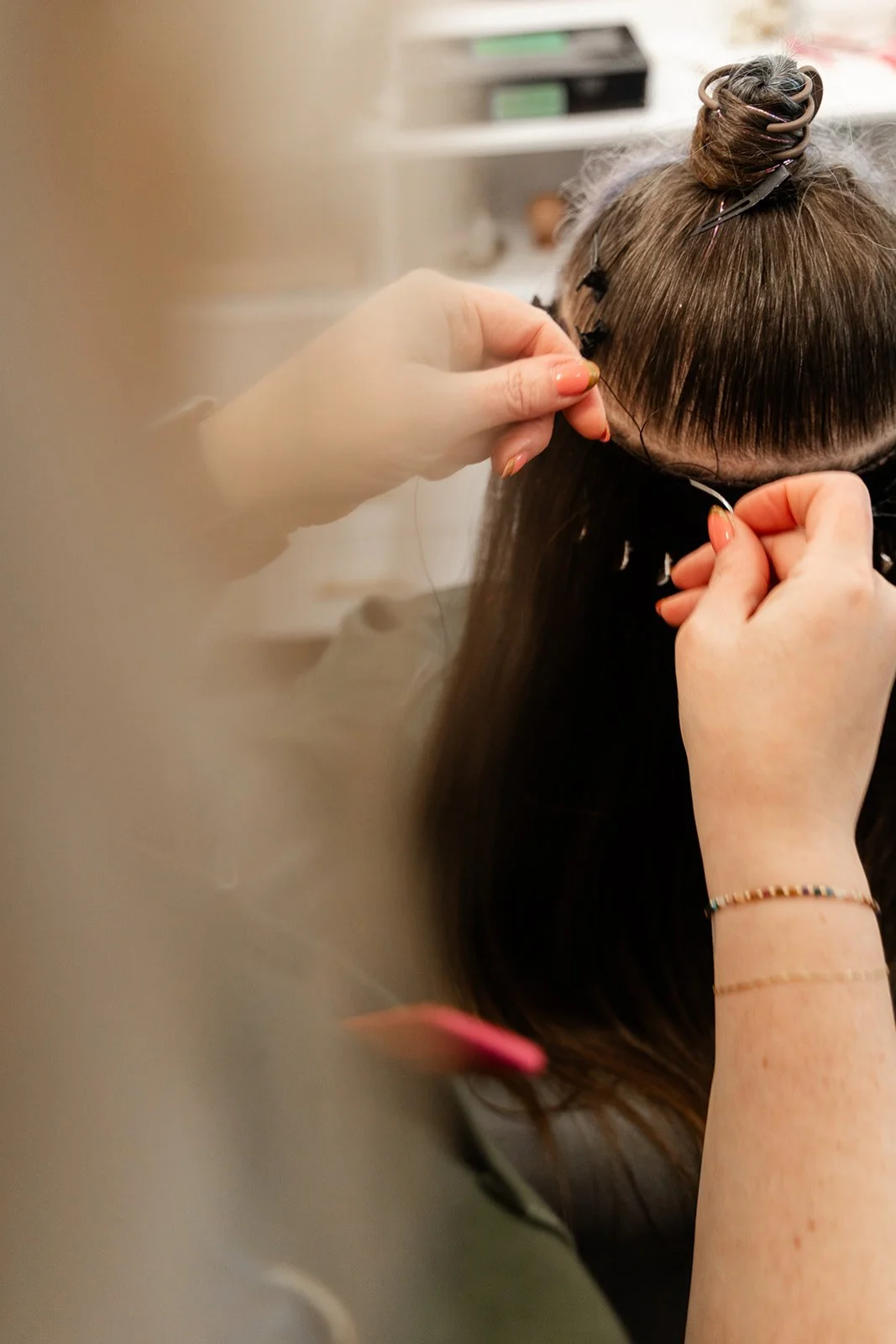 Person getting hair extensions attached by a stylist in a salon.