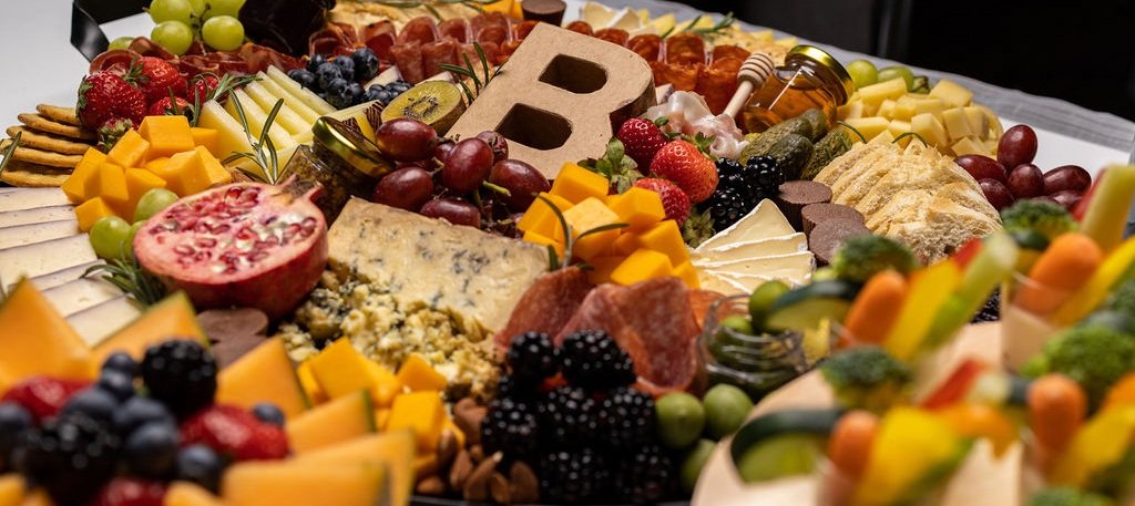 Assorted fruits, cheeses, crackers, and a cheese board, with a decorative letter 'B' in the center.