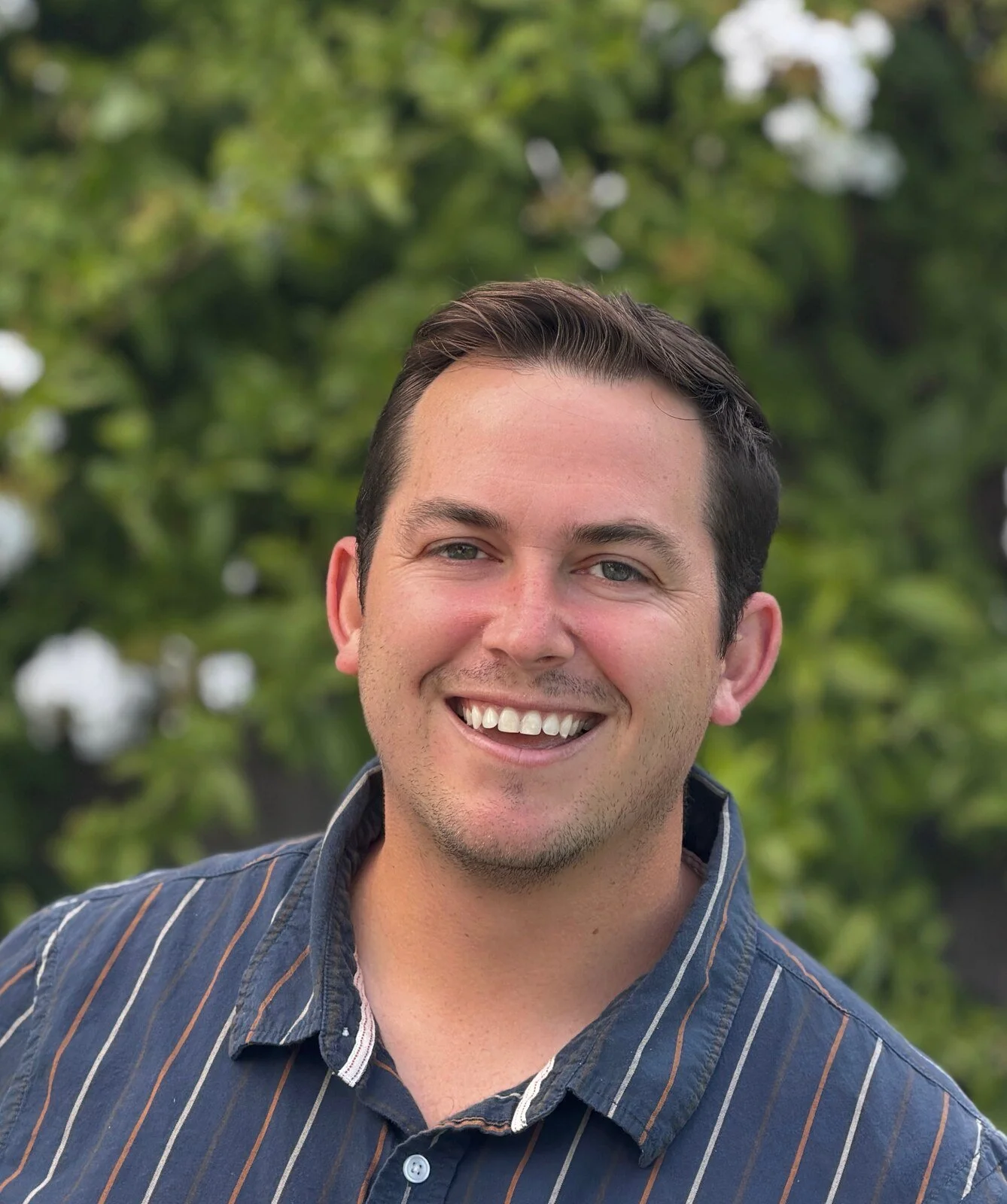 Jake Gorham, associate marriage and family therapist, smiling in a striped navy shirt outdoors among greenery