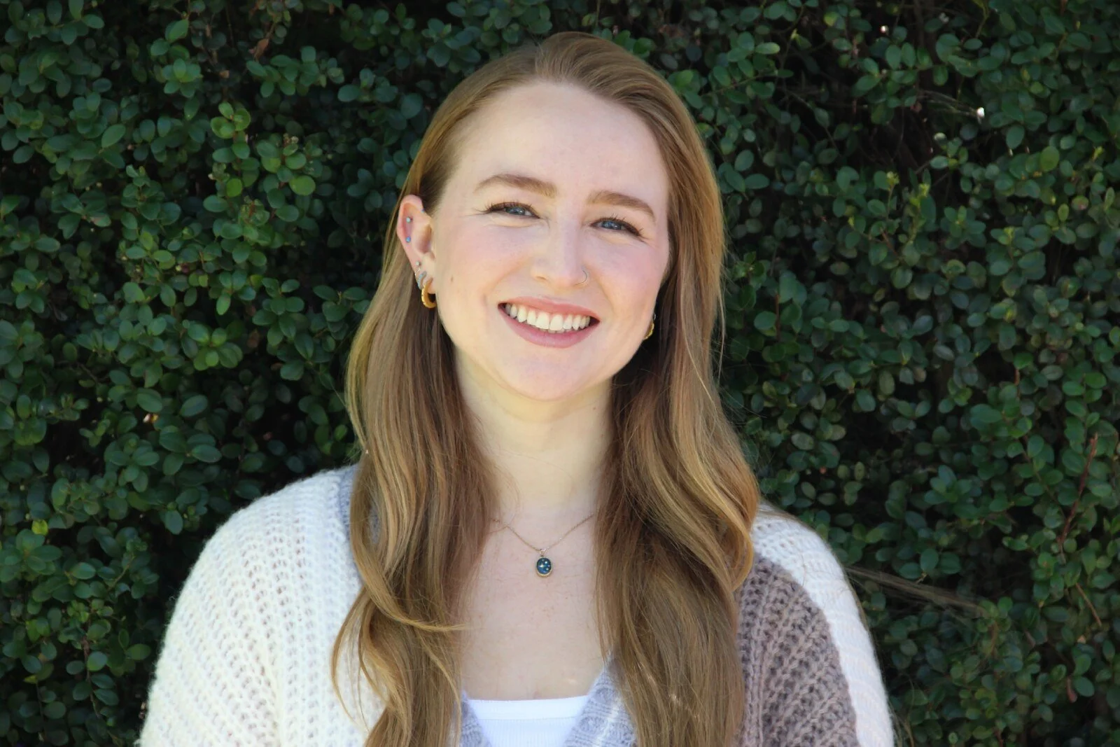 Emma Lewis, associate marriage and family therapist, smiling in a cream cardigan in front of a green hedge