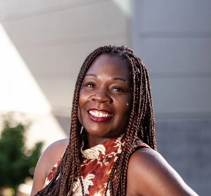 A woman with long braids wearing a floral top, smiling warmly