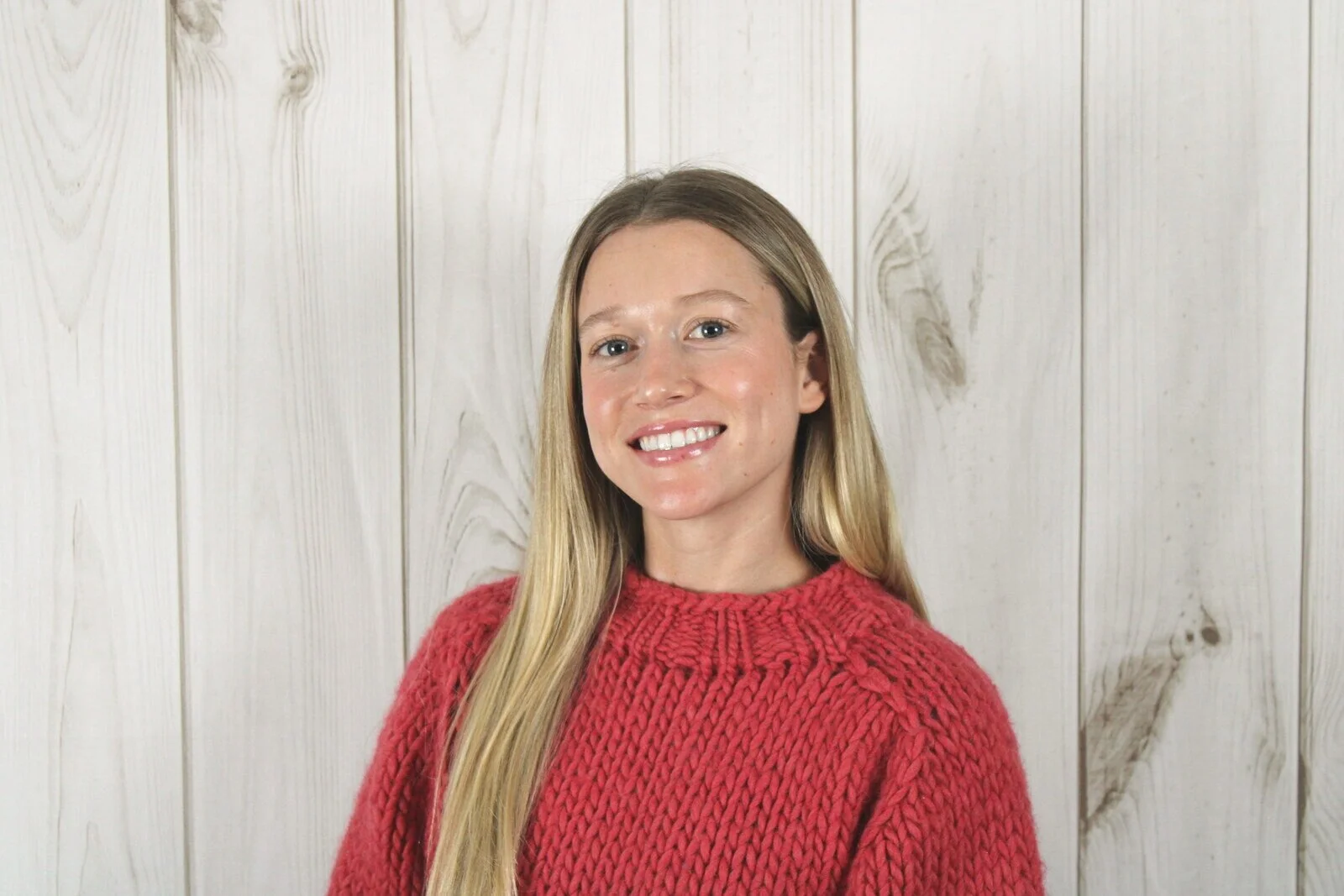 Blake Crawley, associate marriage and family therapist, smiling in a red knit sweater against a whitewashed wood wall