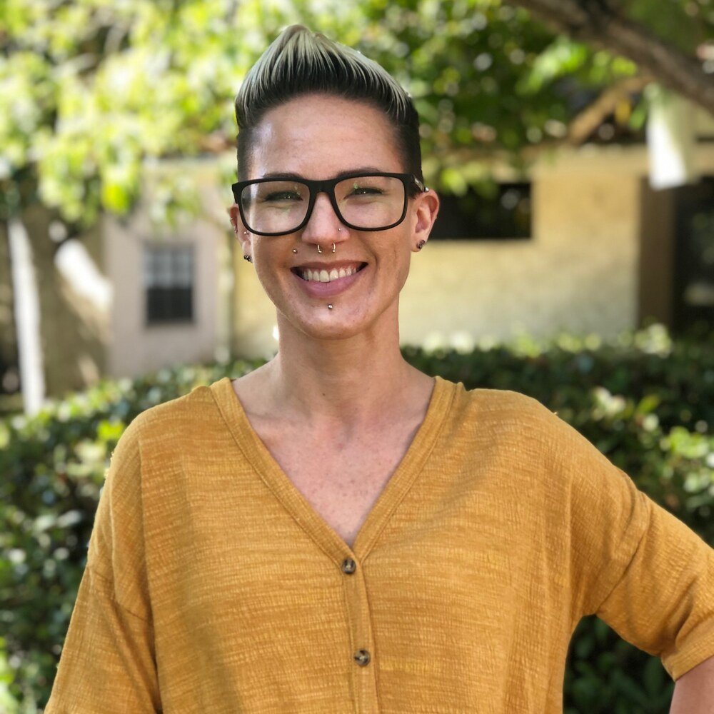 Candace Meridth smiling in a mustard button-up shirt outside under a garden arch