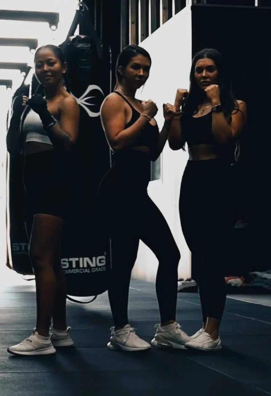 Three women in athletic wear posing with fists up in a gym.