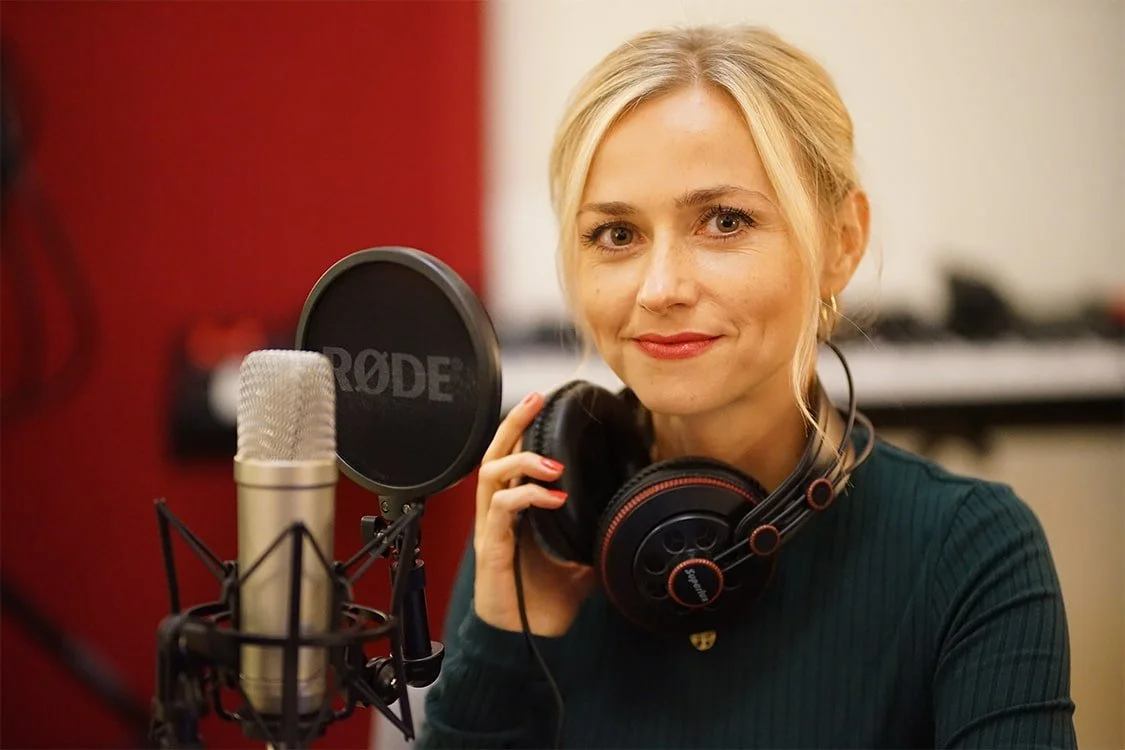 Ira Peter lächelt in die Kamera, sie trägt Kopfhörer und sitzt am Mikrofon