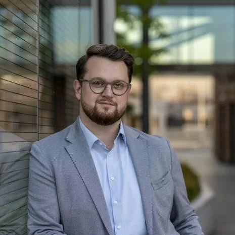 Dietmar Schulmeister steht angelehnt an einer Wand und lächelt leicht in die Kamera. 