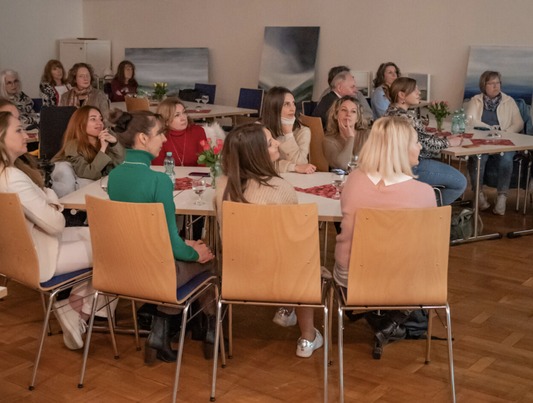 Eine Gruppe von Menschen sitzt in einem Saal und hört aufmerksam zu.
