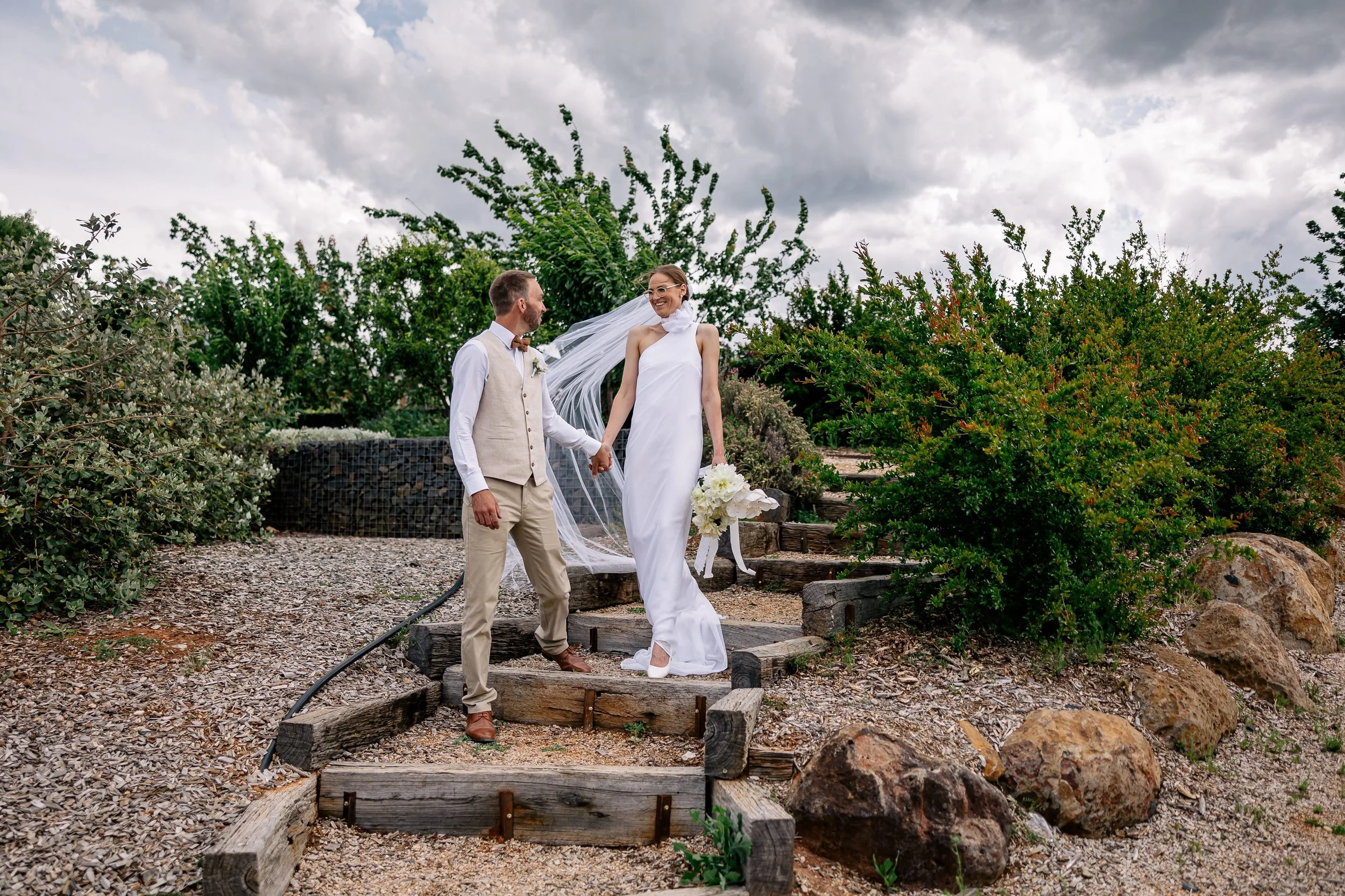 A bride and groom kissing outdoors at night under a starry sky, surrounded by manicured bushes with small string lights.