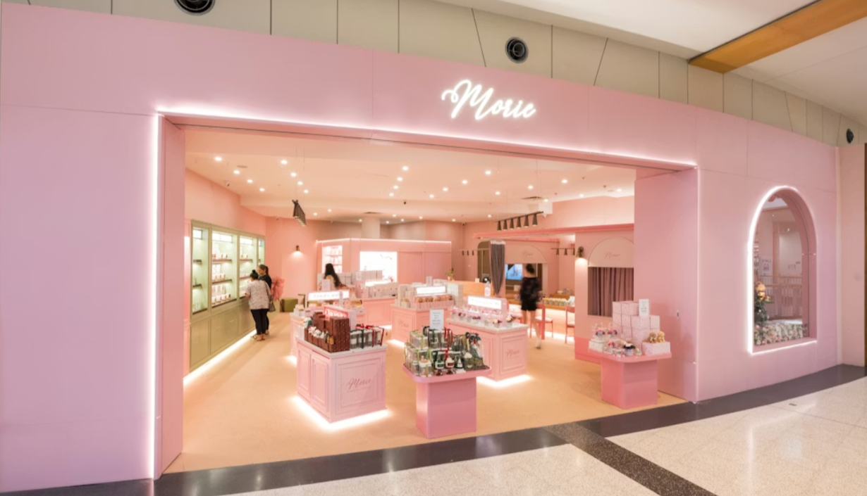 A pink retail store with display counters and shelves, decorated in a pastel theme, selling various products, with customers shopping inside.