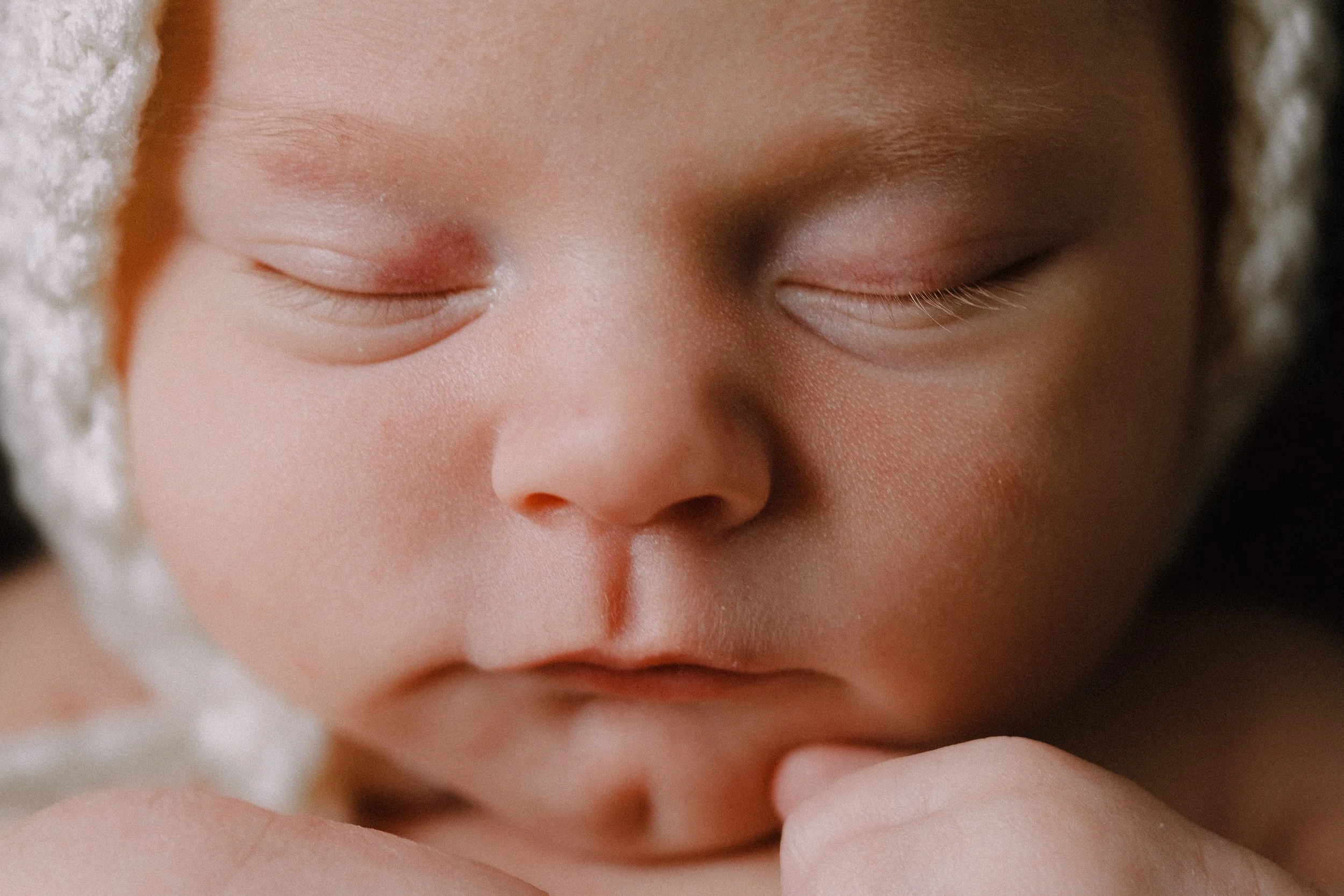 Newborn baby, close up of face wearing a knit bonnet.