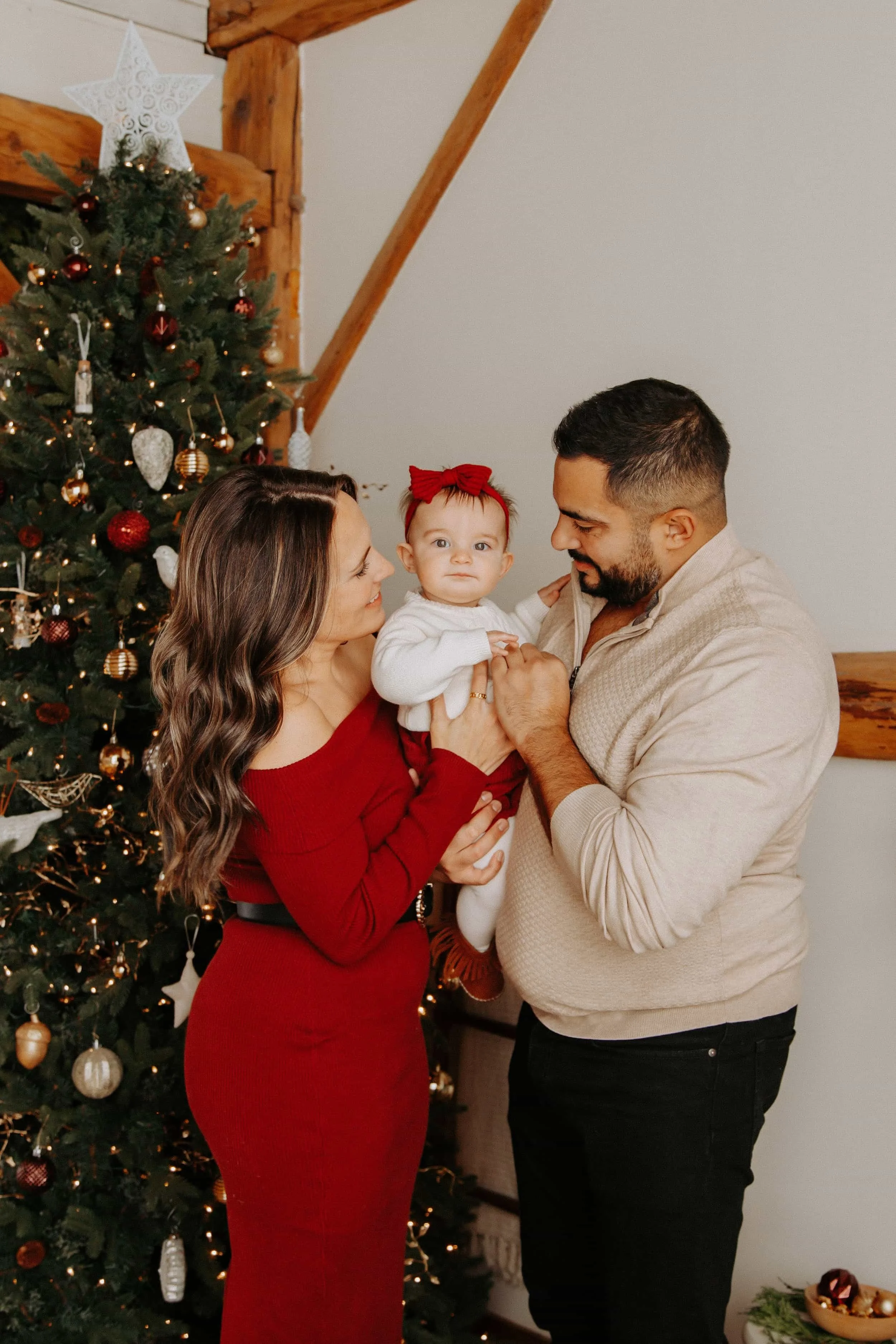 Family of three standing in front of a Christmas tree.