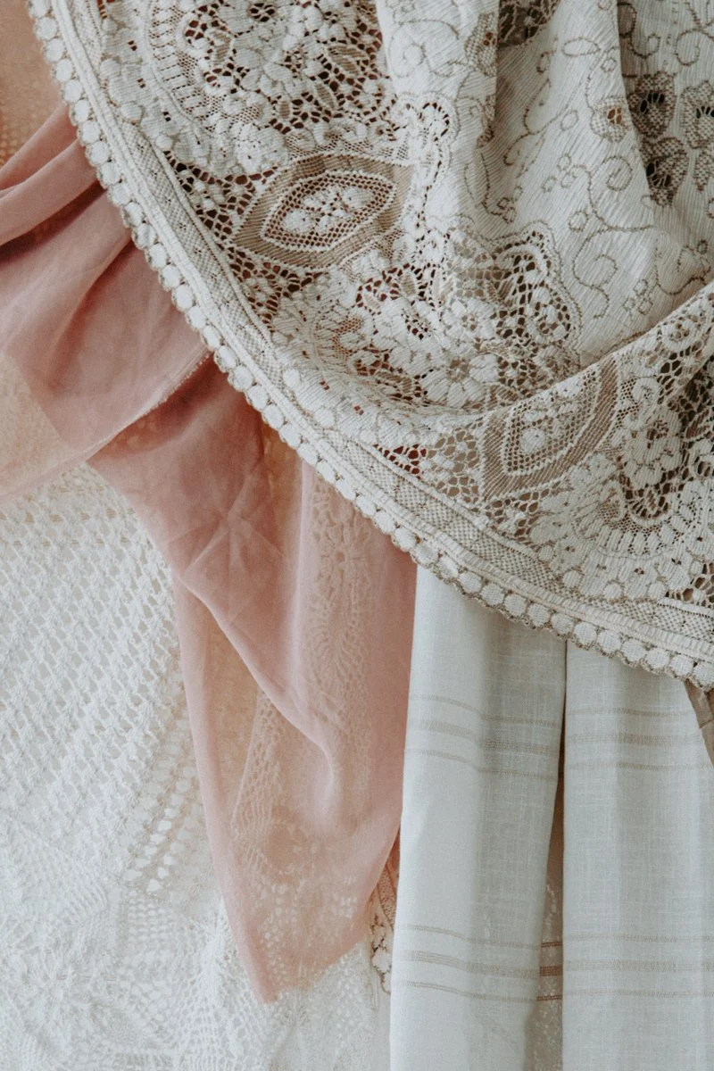 Close-up of various lace and fabric textiles in neutral and pastel colors.