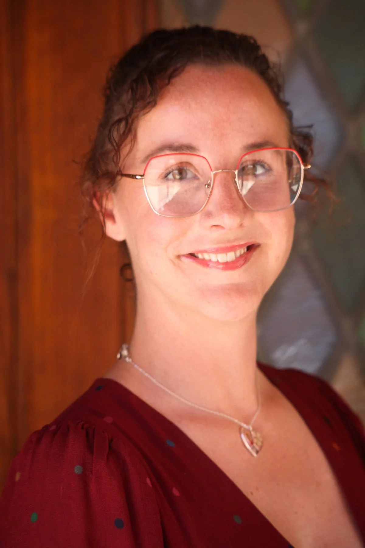 A photograph shows a young woman with curly hair who is wearing glasses and smiling