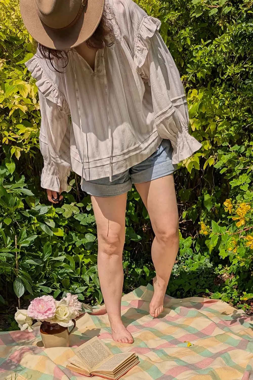 Loose cream peasant blouse with romantic shoulder ruffles and long cuffed sleeves worn in a sunlit garden.