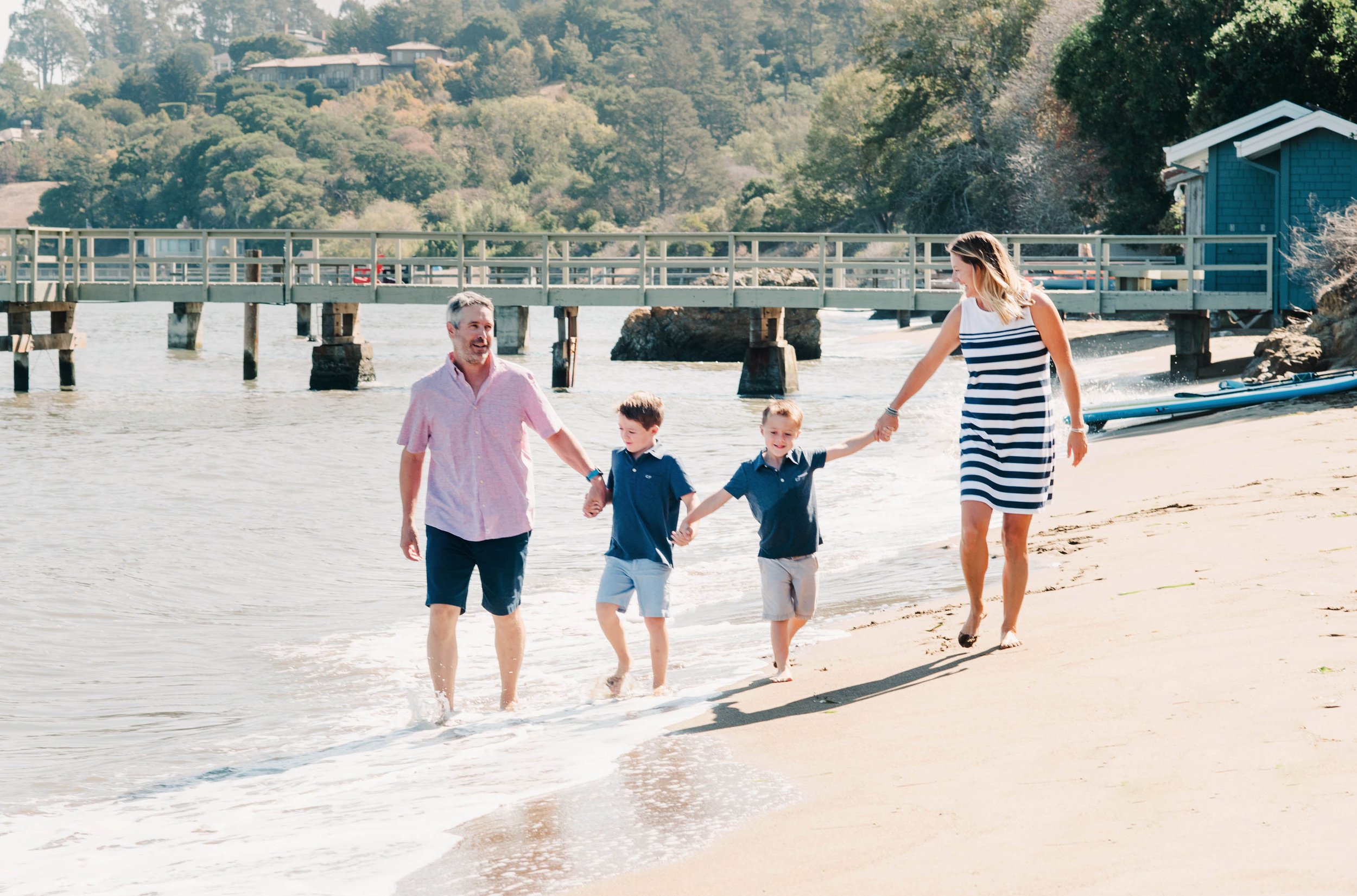 Family of four walking on a beach near a pier, in Tiburon, Ca, holding hands. Family photo session.