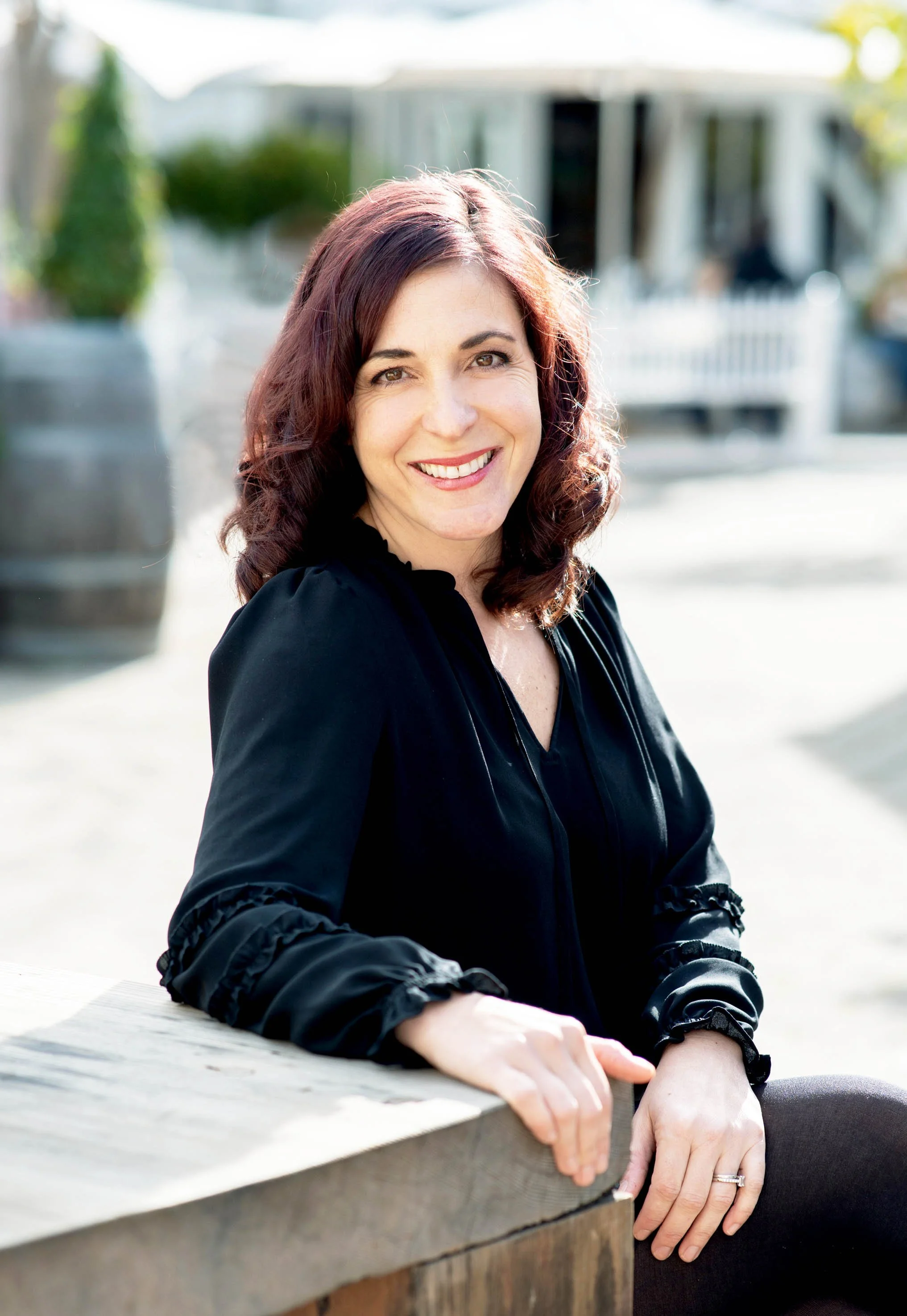 Smiling woman with curly hair, wearing a black blouse, posing outdoors.