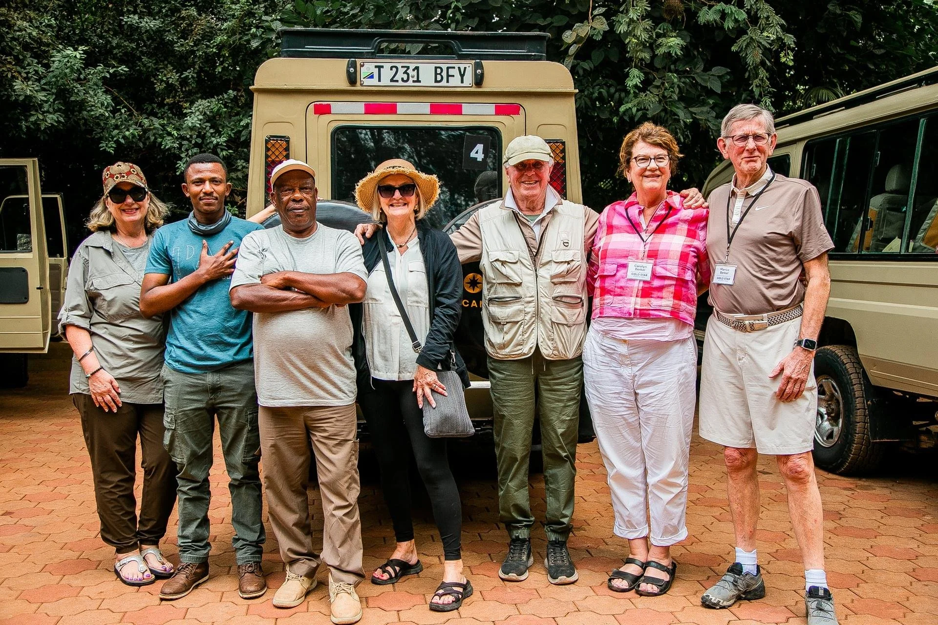 Group of eight tourists standing in front of safari vehicles in a lush green jungle setting, smiling and preparing for a safari tour.