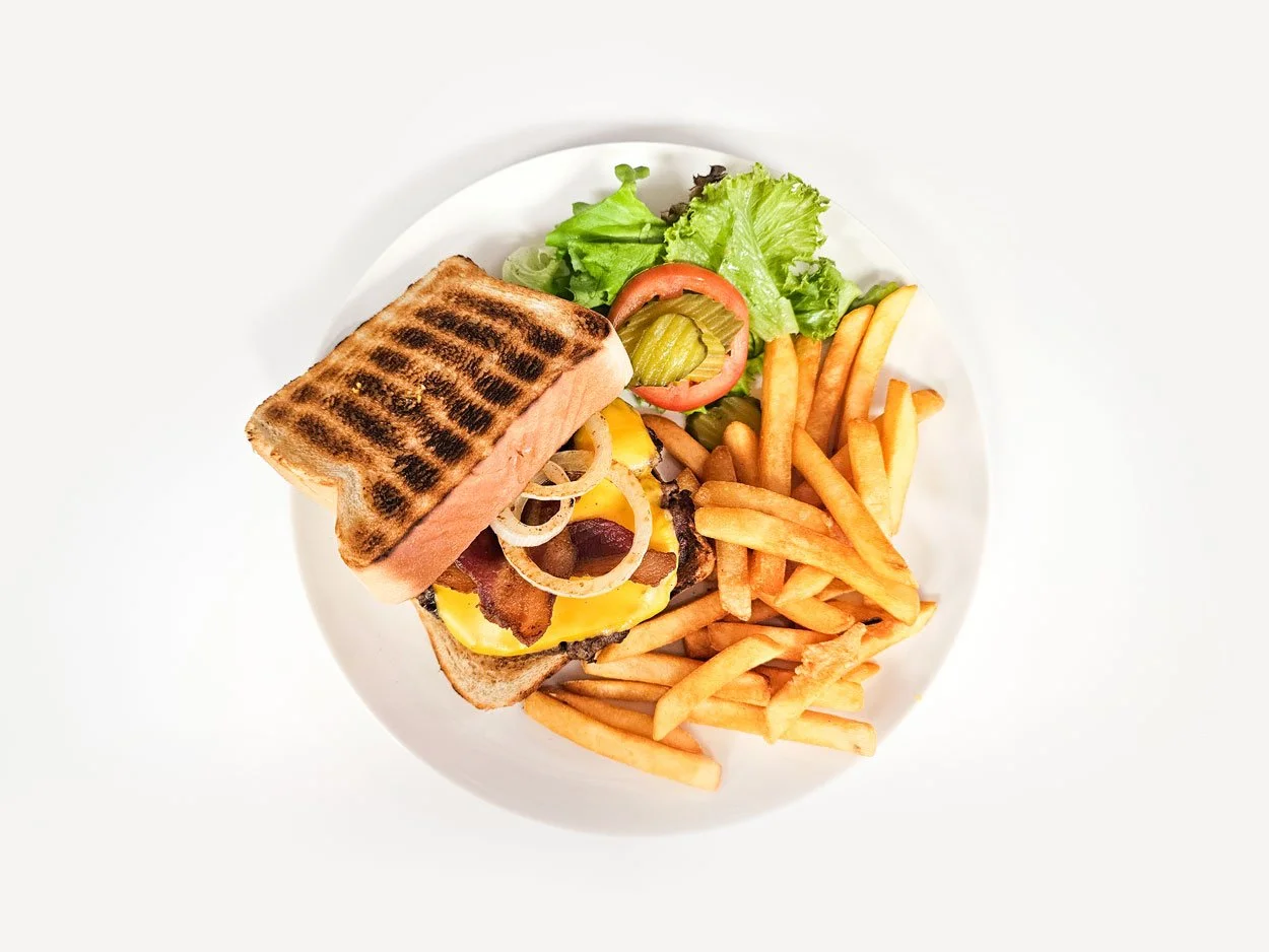 Plate with a grilled salmon sandwich burger, fries, and fresh salad with lettuce, tomato, and pickles.