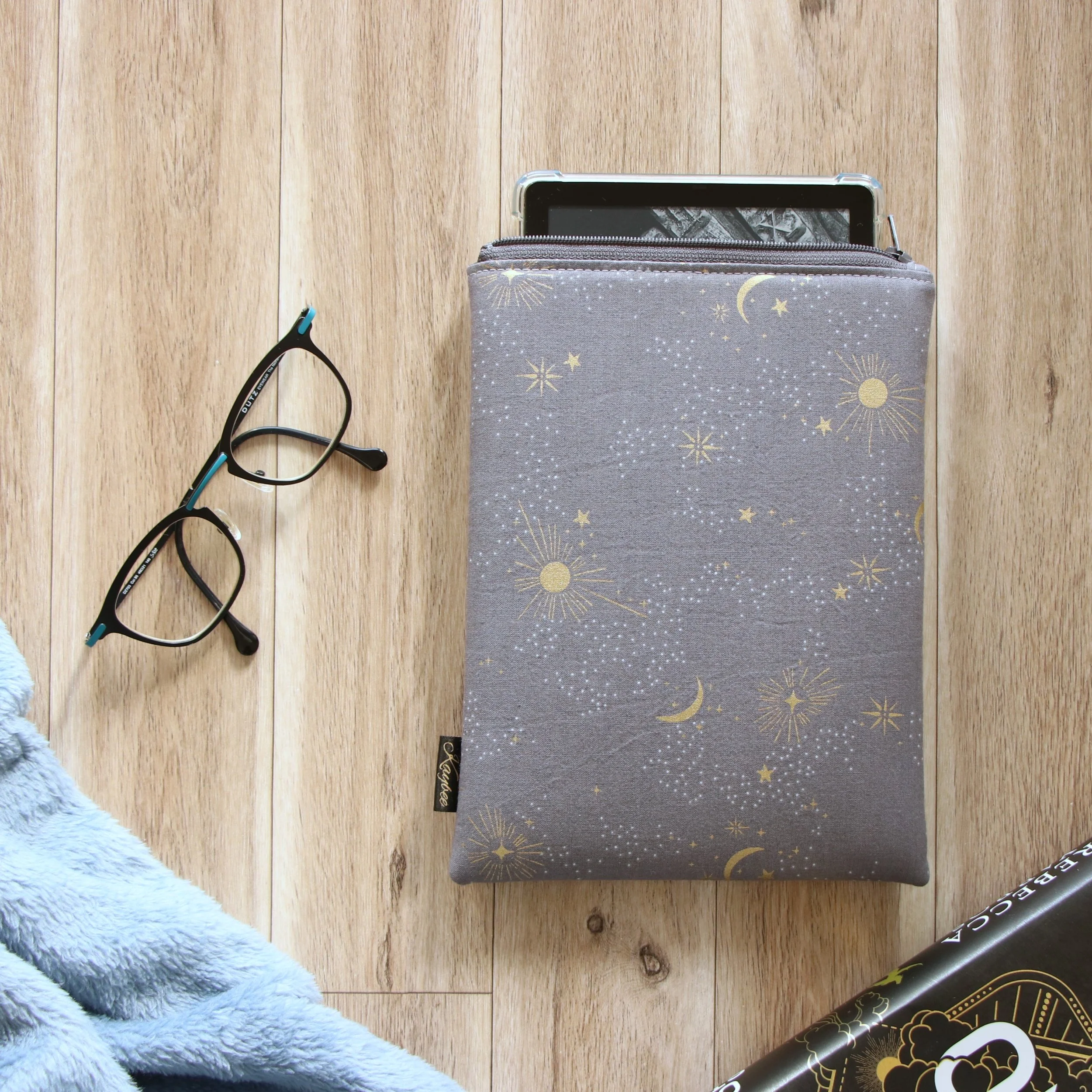 Handmade First Edition Kindle Sleeve with dragon-inspired fabric beside book and reading accessories.