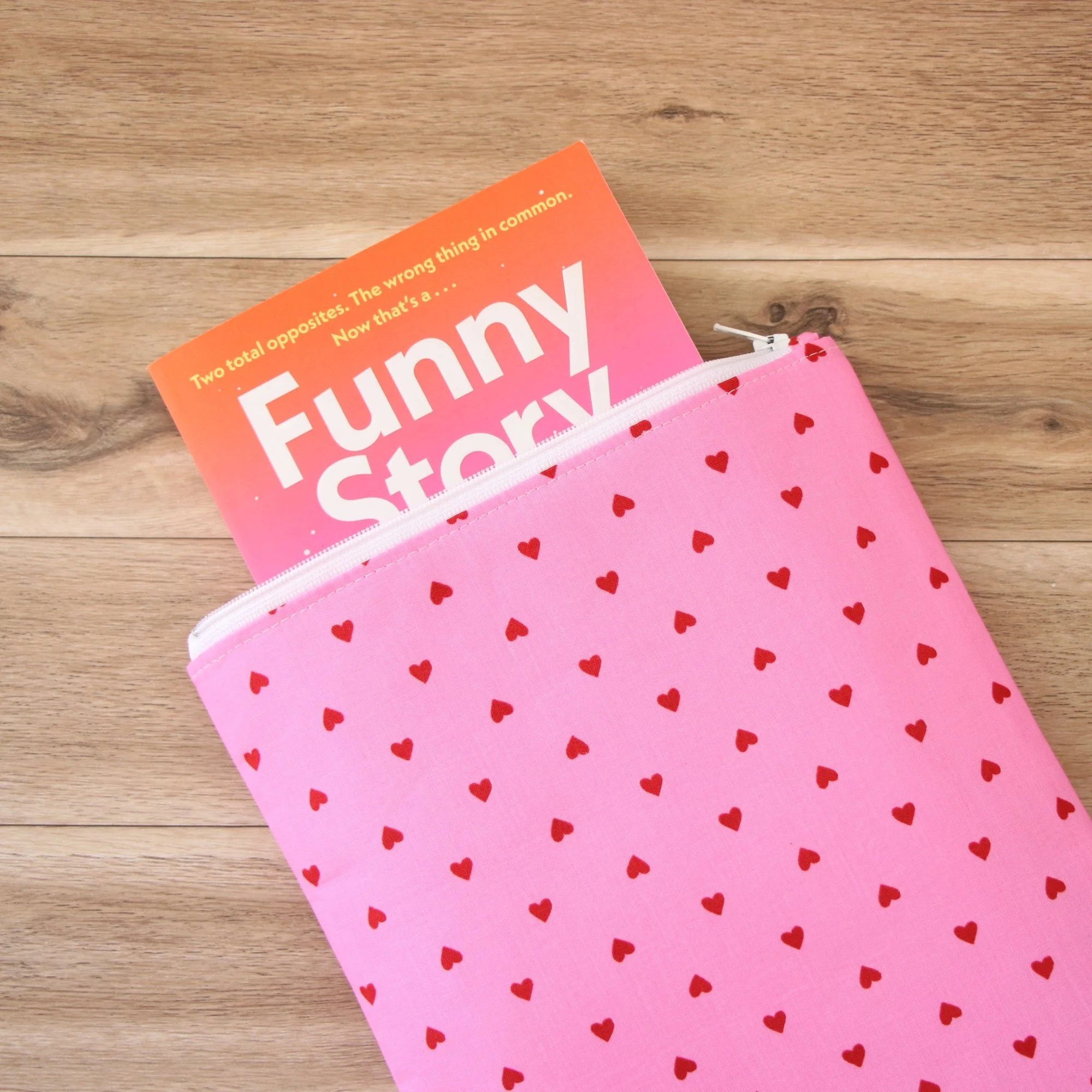Classic Book Sleeve in pink heart print fabric showing a paperback partially inside the zippered sleeve.
