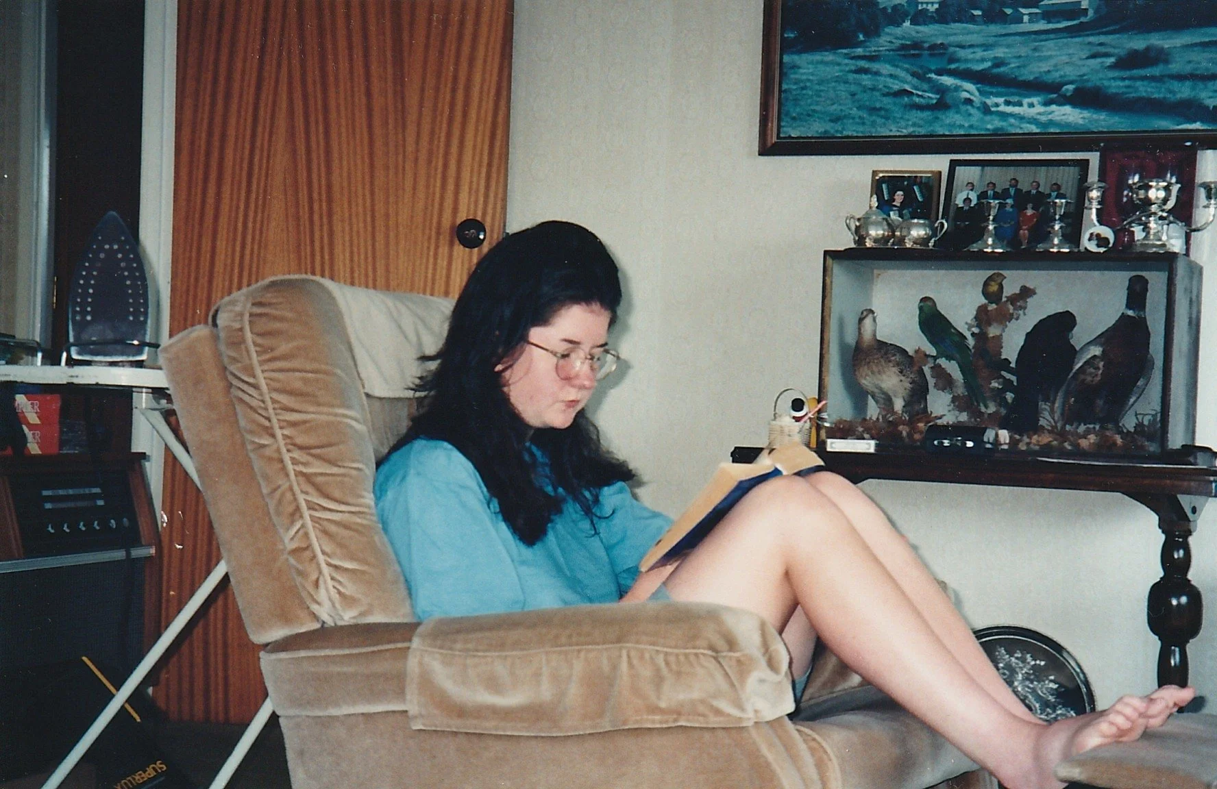 1990s teenage book nerd wearing glasses reading a book in a lazyboy chair.