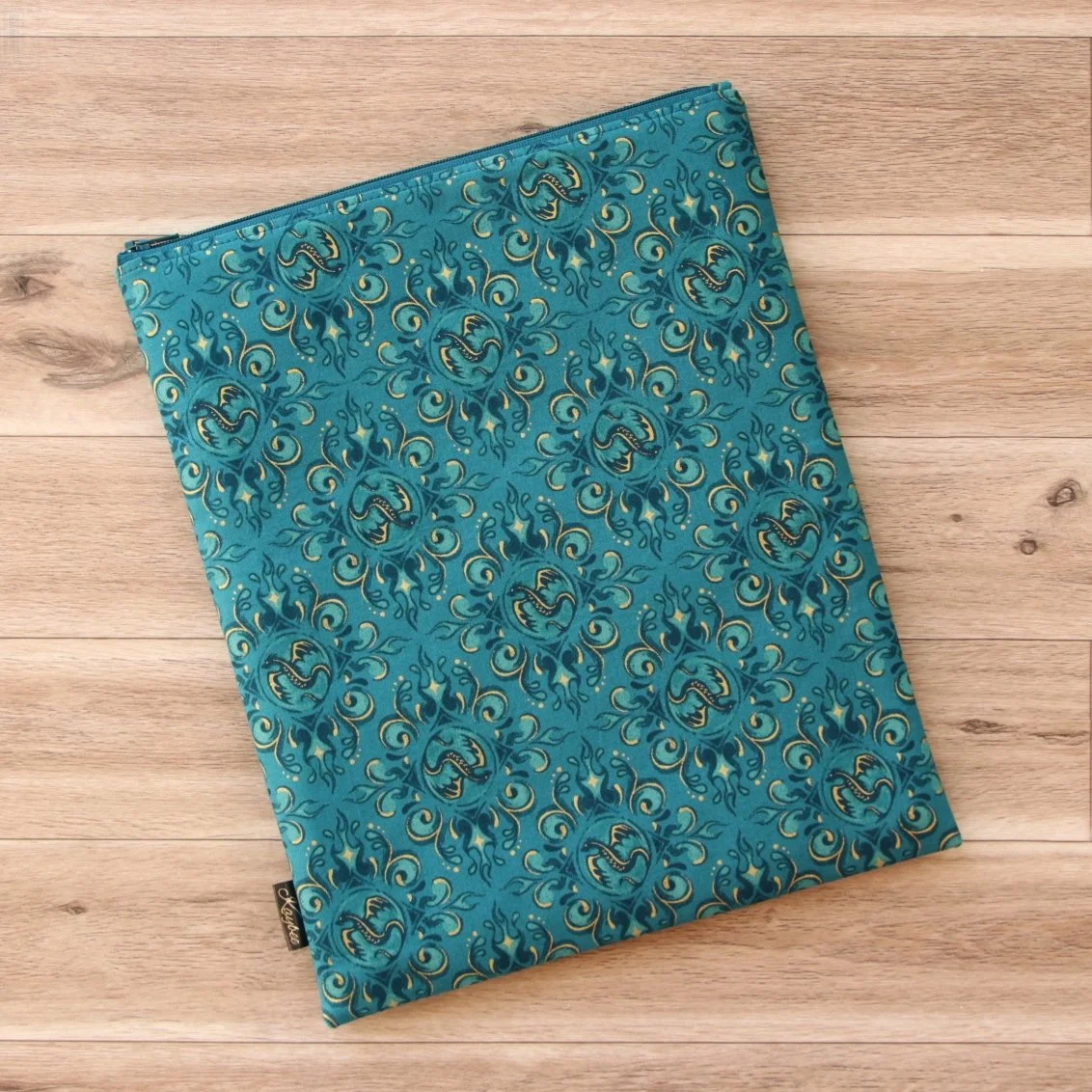 Large handmade dragon book sleeve in teal designer fabric with a premium YKK zip on a wooden background.