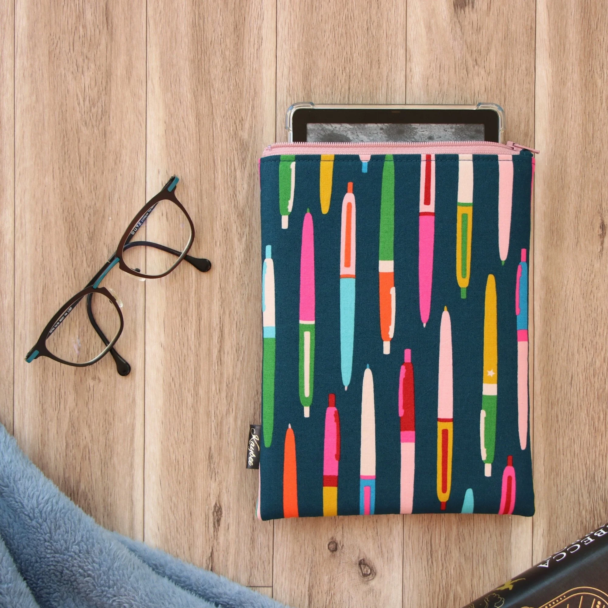 Handmade First Edition Kindle Sleeve with pens fabric beside book and reading accessories.