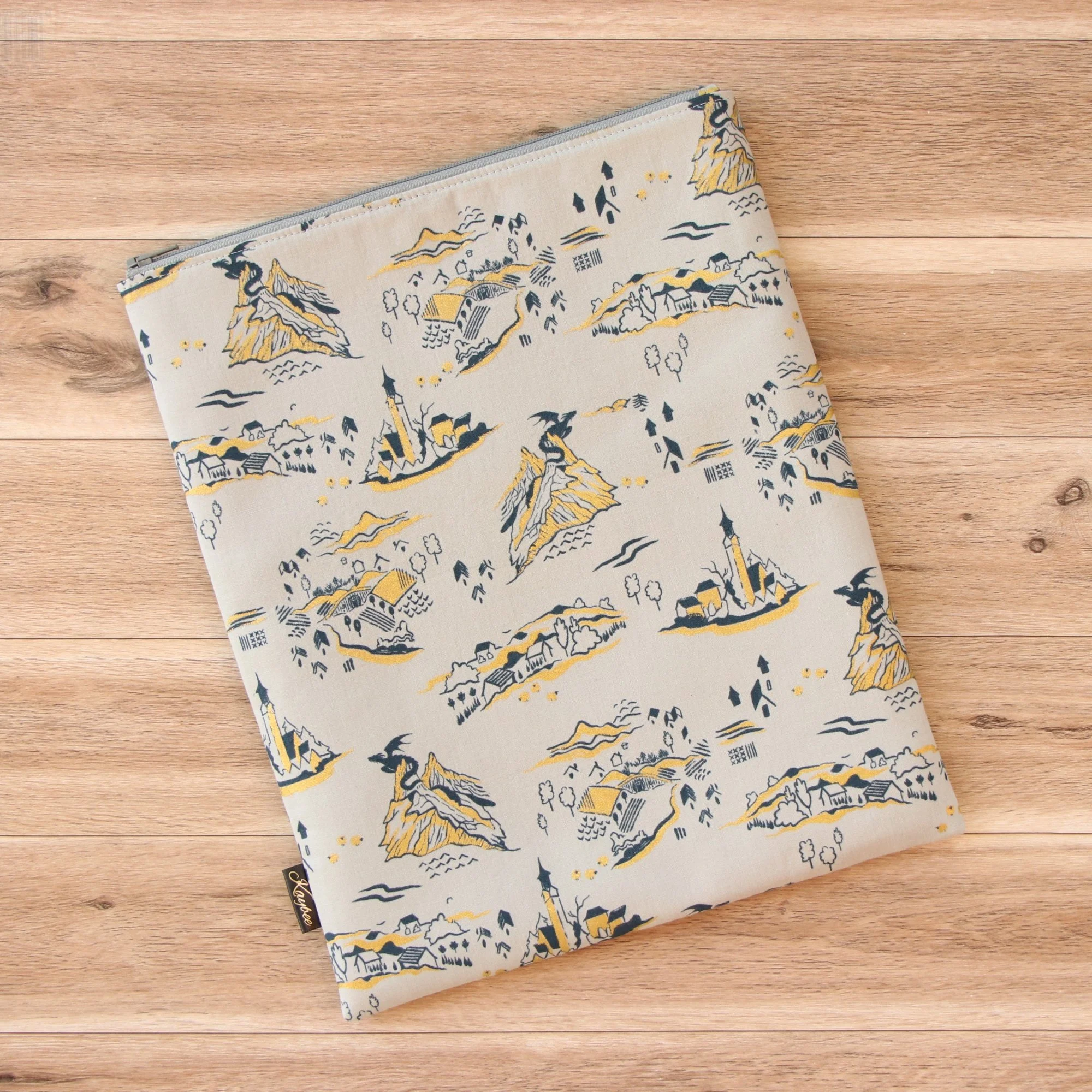 Large handmade fantasy book sleeve in gray designer fabric with a premium YKK zip on a wooden background.