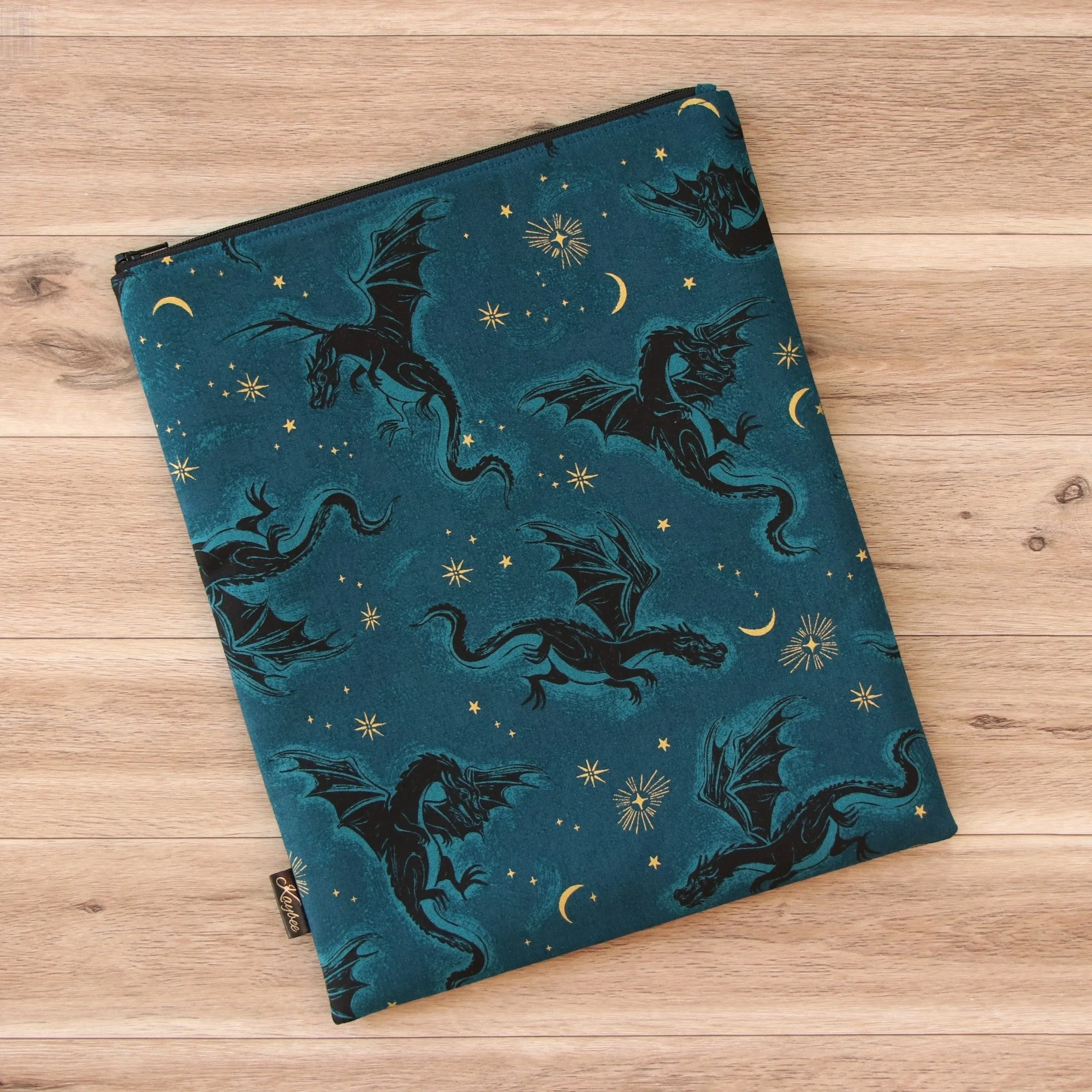 Large handmade dragon book sleeve in teal designer fabric with a premium YKK zip on a wooden background.