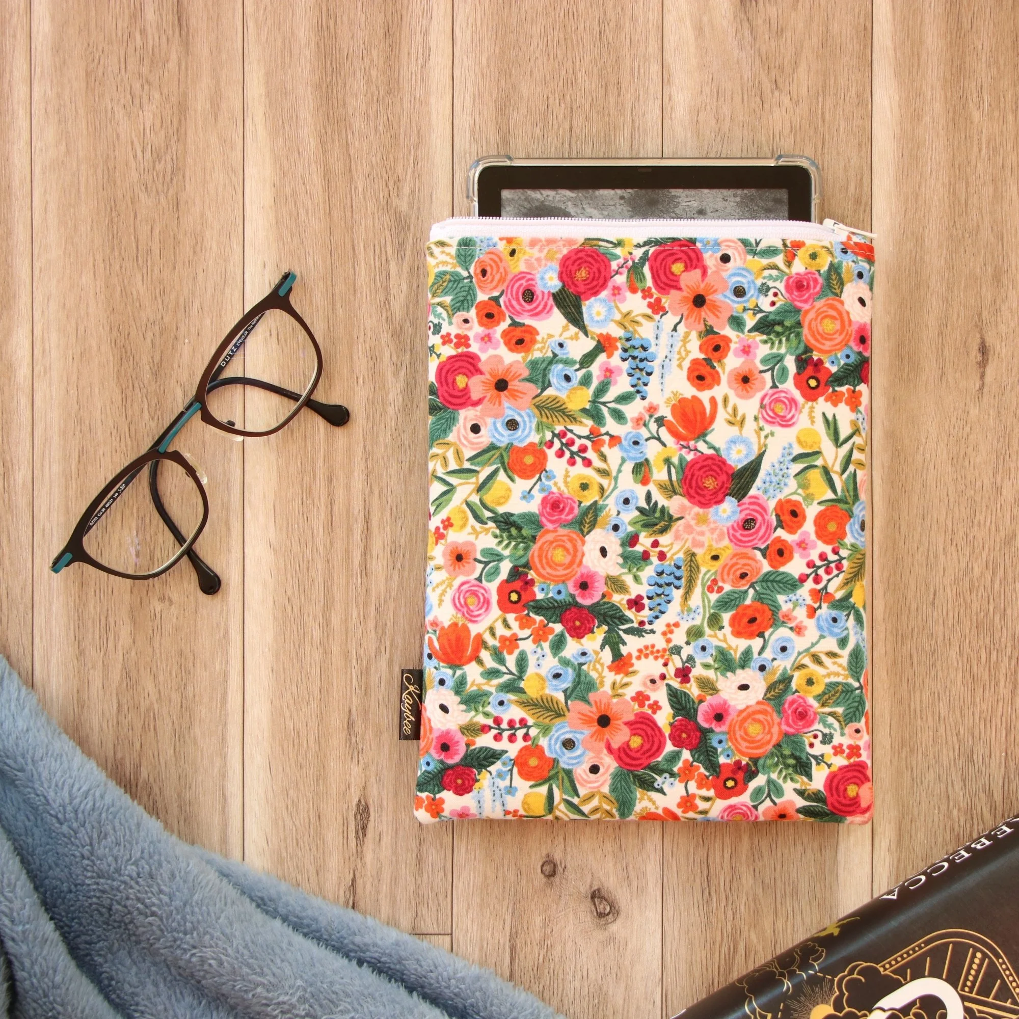 Handmade First Edition Kindle Sleeve with floral fabric beside book and reading accessories.