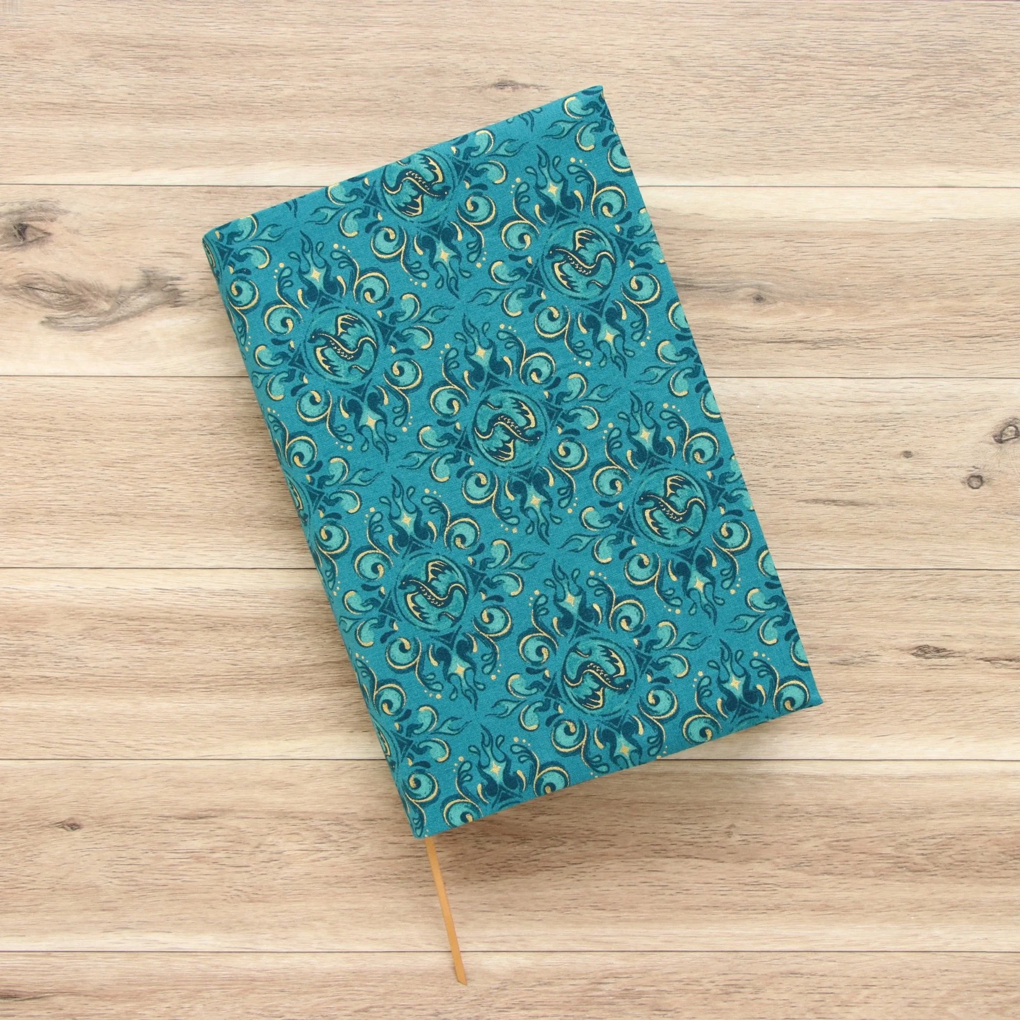 Handmade adjustable fabric book jacket protecting a hardcover book with dragon-inspired fabric.