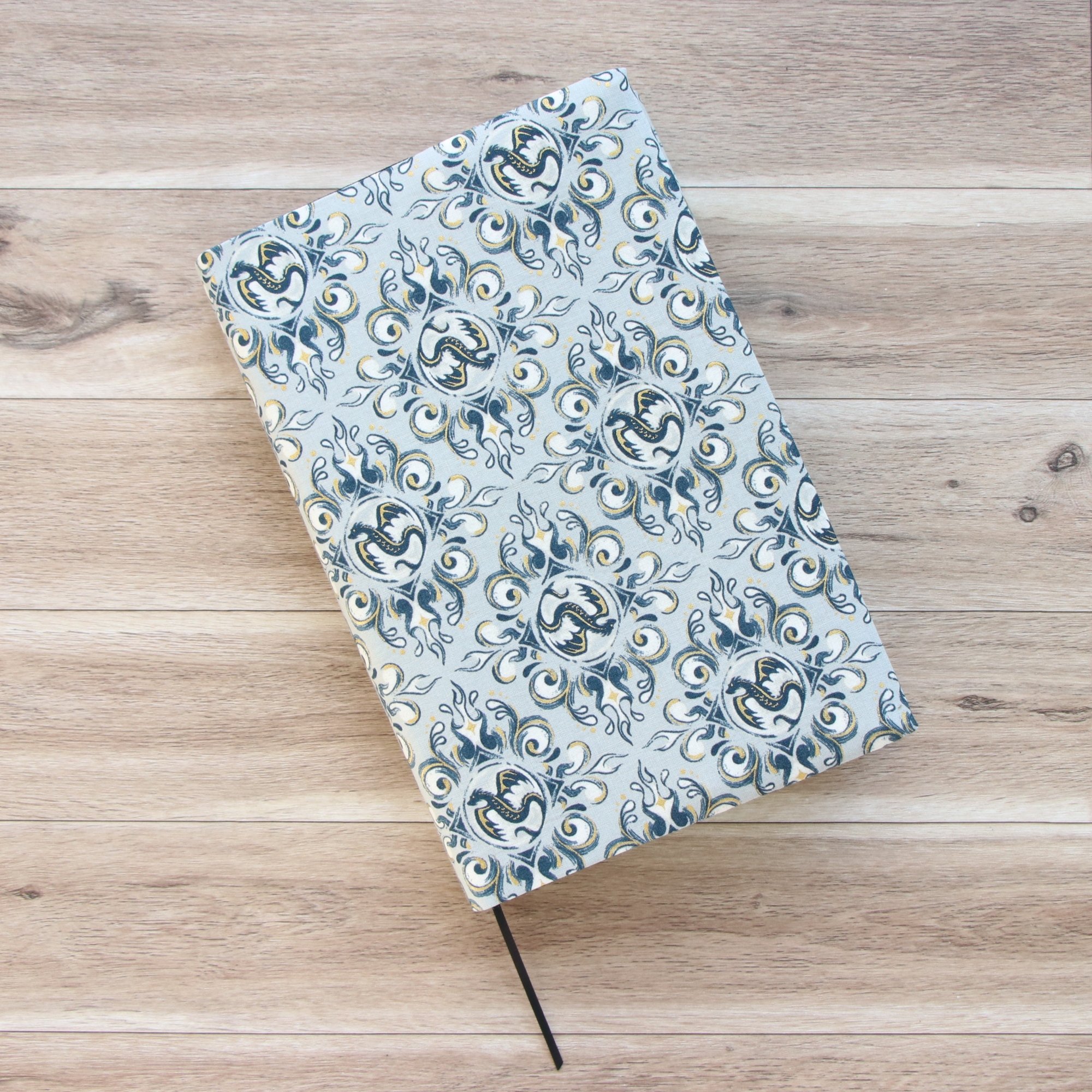 Handmade adjustable fabric book jacket protecting a hardcover book with dragon-inspired fabric.