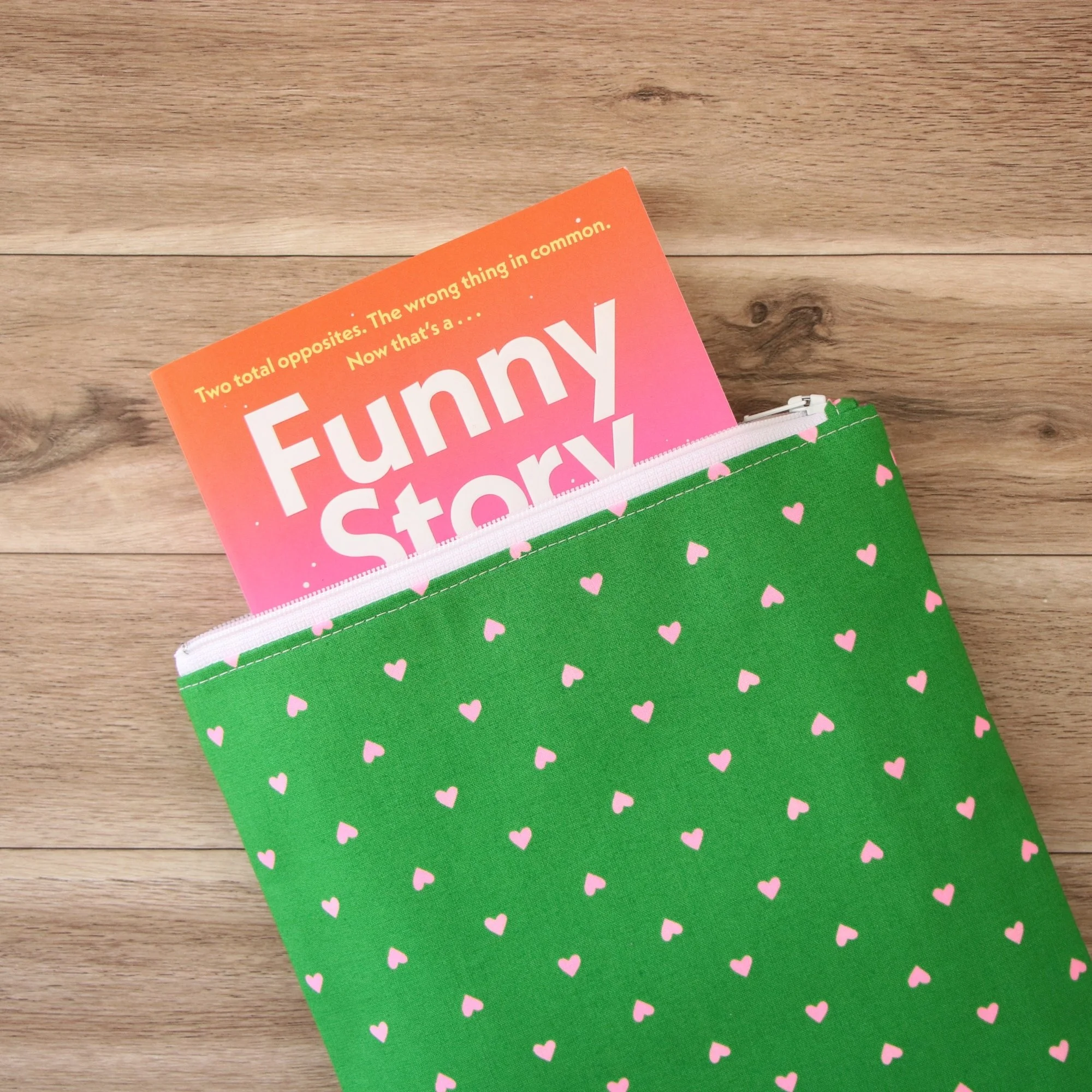 Classic Book Sleeve in green heart print fabric showing a paperback partially inside the zippered sleeve.