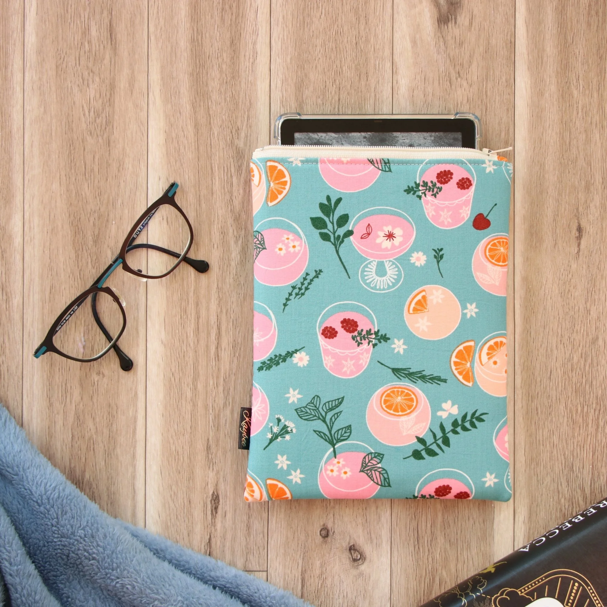 Handmade First Edition Kindle Sleeve with cocktail-inspired fabric beside book and reading accessories.