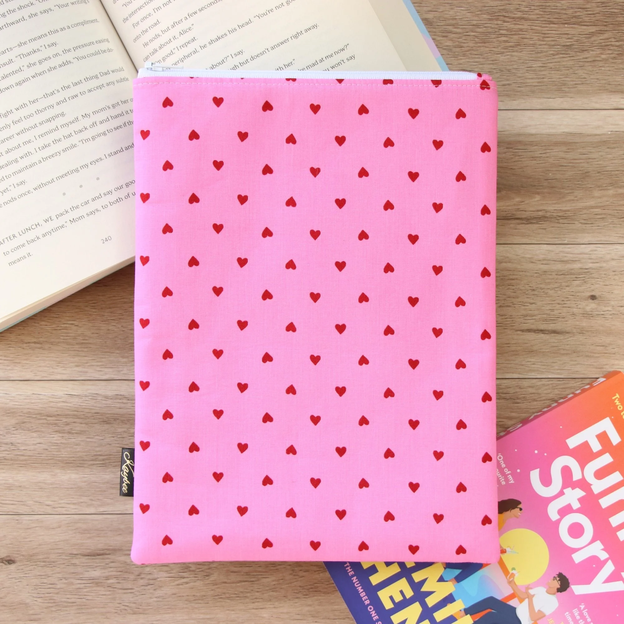 Handmade Classic Book Sleeve in pink fabric with red hearts photographed beside an open book.