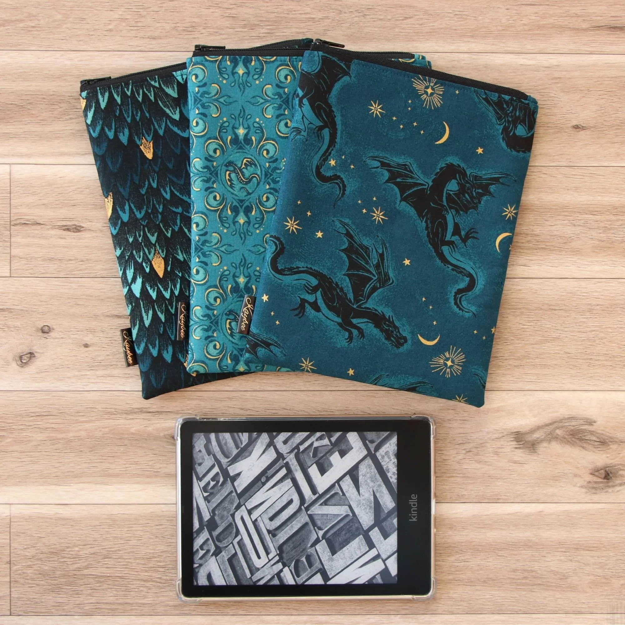 Three handmade fabric Kindle Sleeves in fantasy-inspired dragon fabrics with a Kindle e-reader, handcrafted in New Zealand.