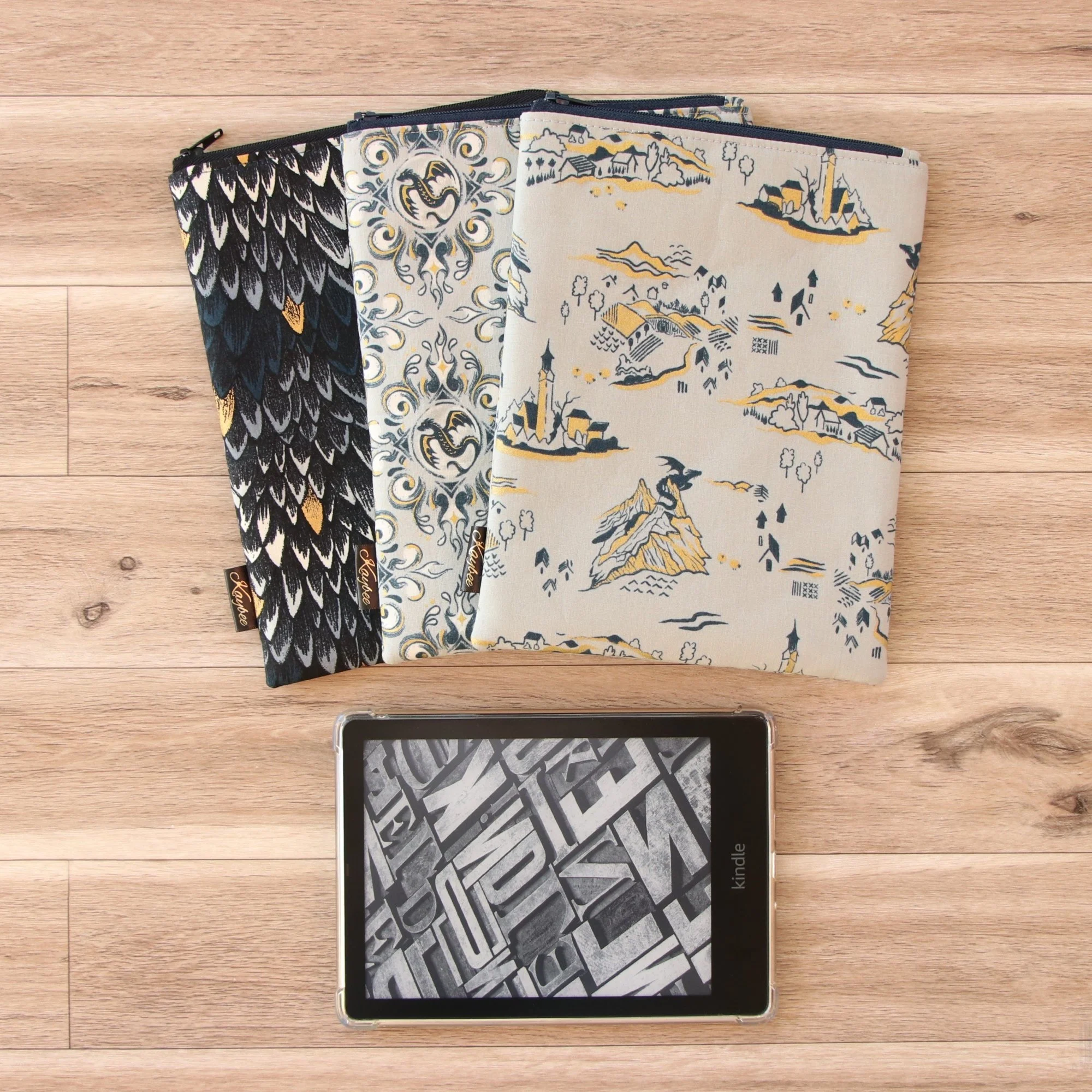 Three handmade fabric Kindle Sleeves in fantasy-inspired dragon fabrics with a Kindle e-reader, handcrafted in New Zealand.
