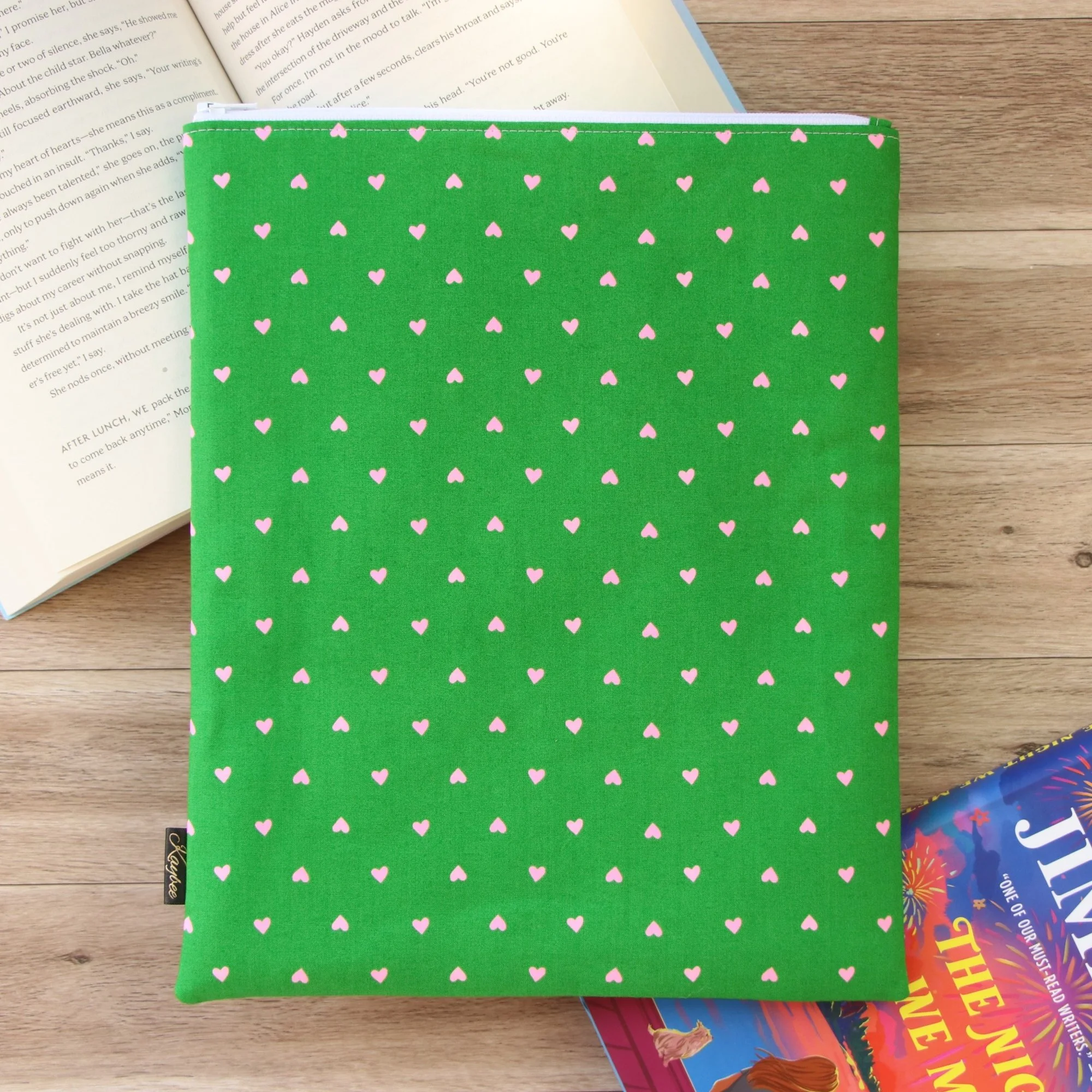 Handmade Classic Book Sleeve in green fabric with pink hearts photographed beside an open book.