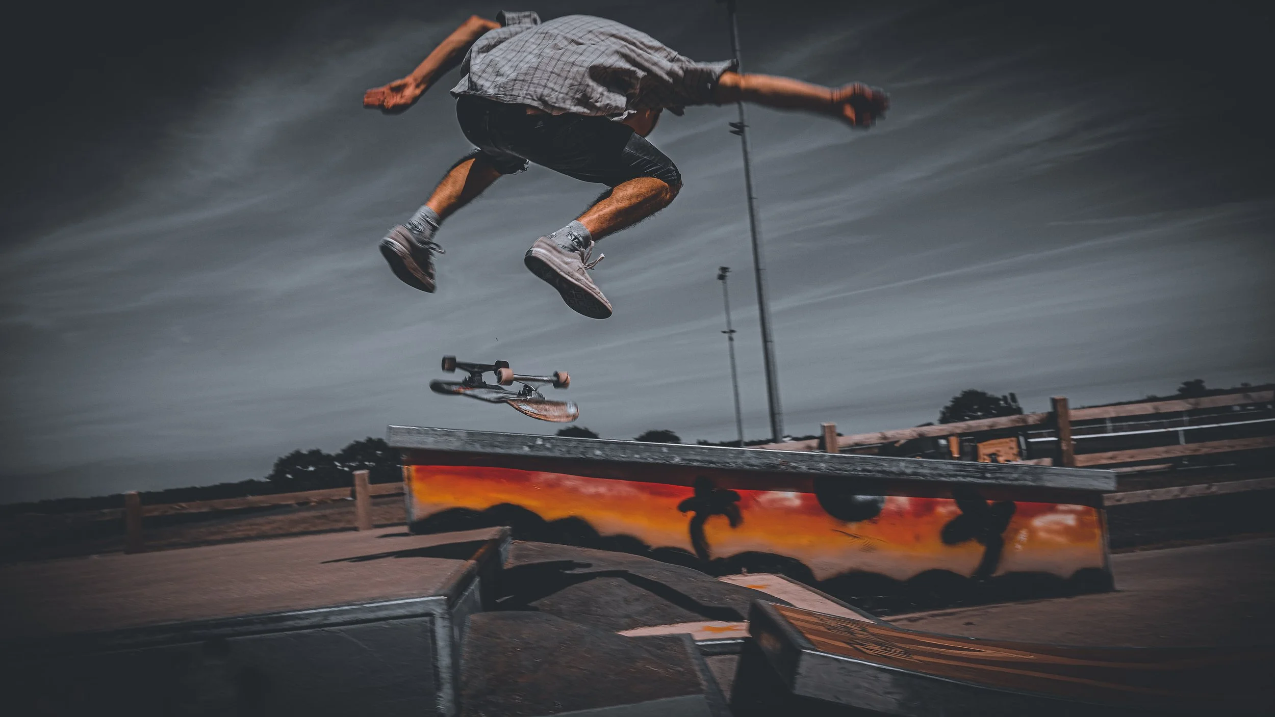 A skateboarder performing a mid-air trick at a skate park during a cloudy day.