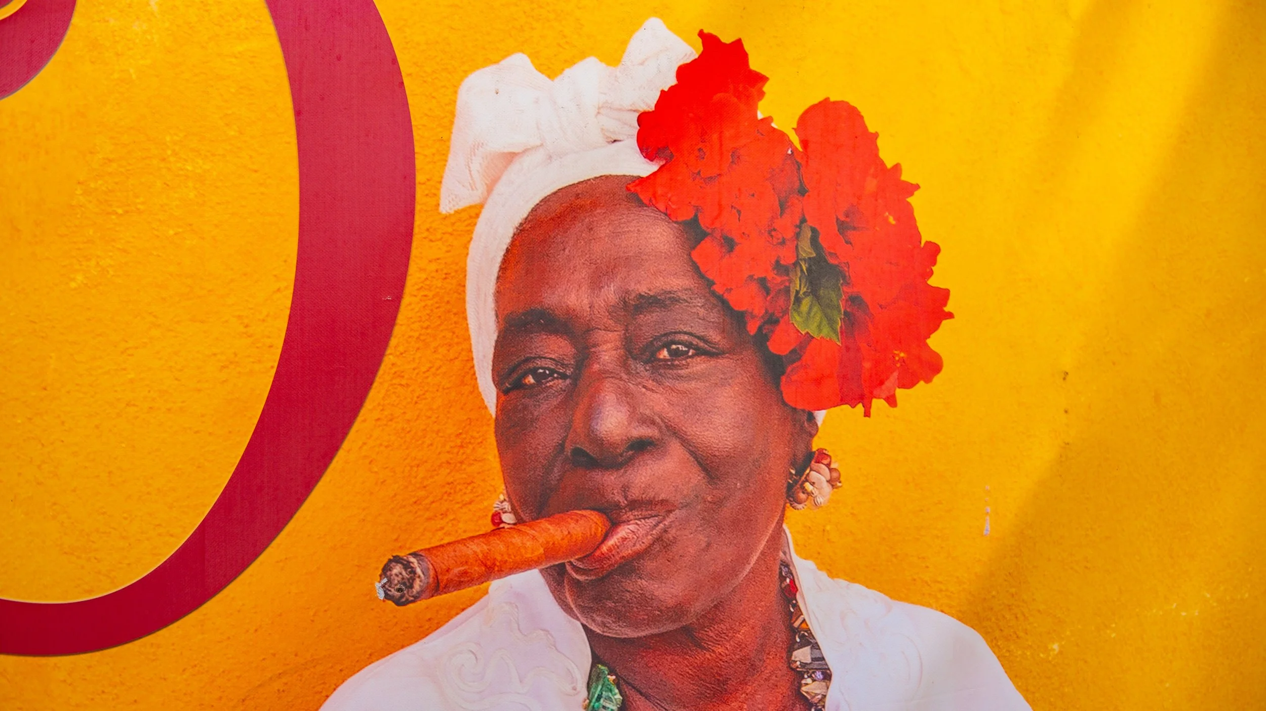 A woman wearing a white headwrap, red flower adornment, earrings, and a white top, smoking a cigar, against a vibrant yellow background.